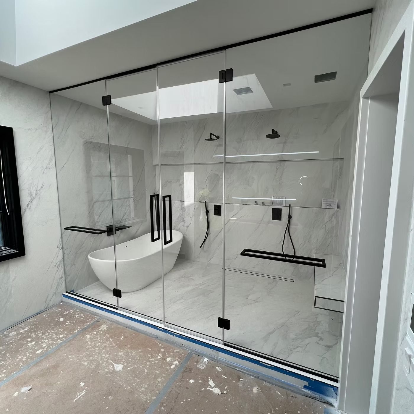 Modern bathroom with glass shower enclosure, white marble walls, and freestanding tub under renovation