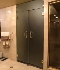 Dark double doors in a beige hallway with towels on the left and a glass door on the right
