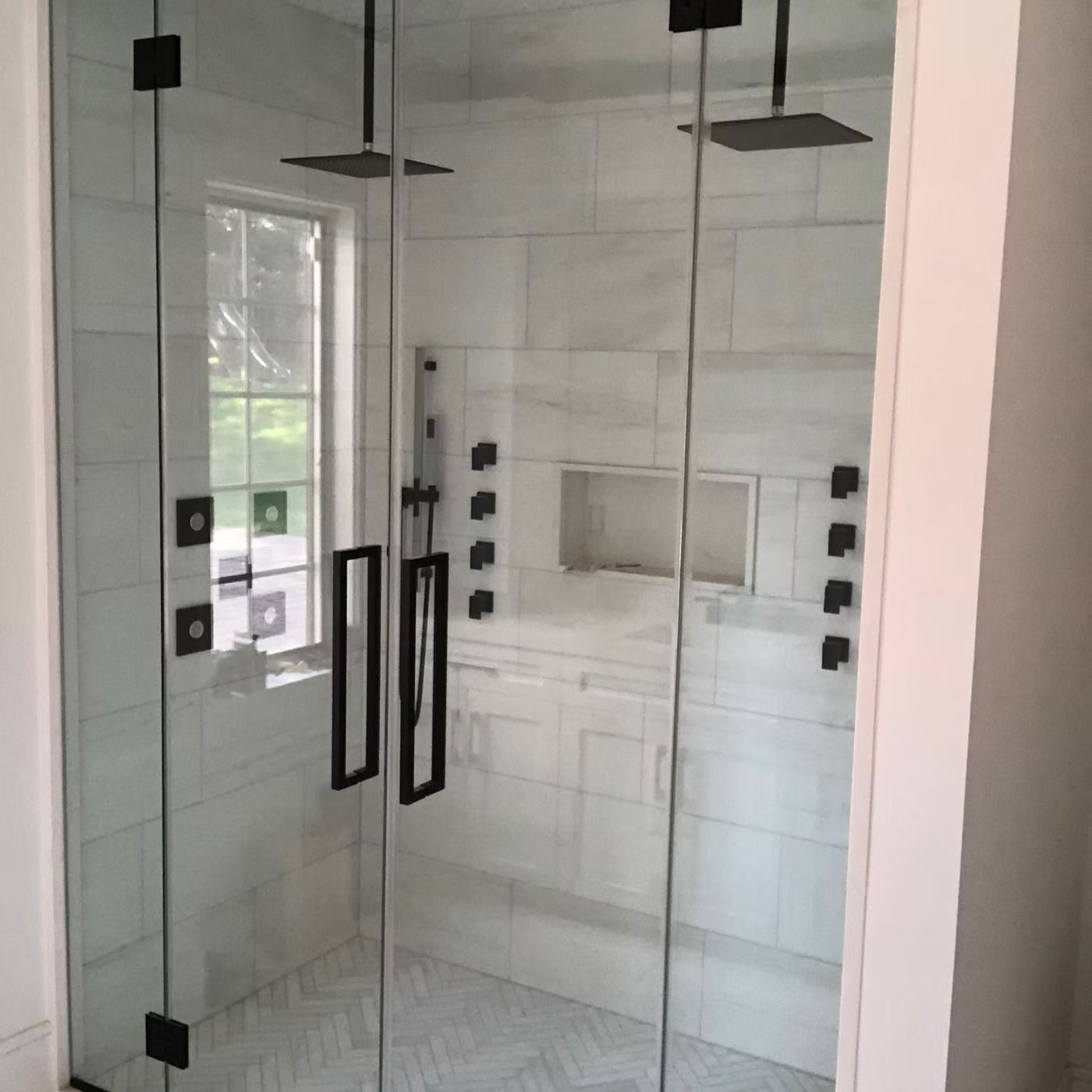 Glass shower with black hardware and white tile in a bright bathroom