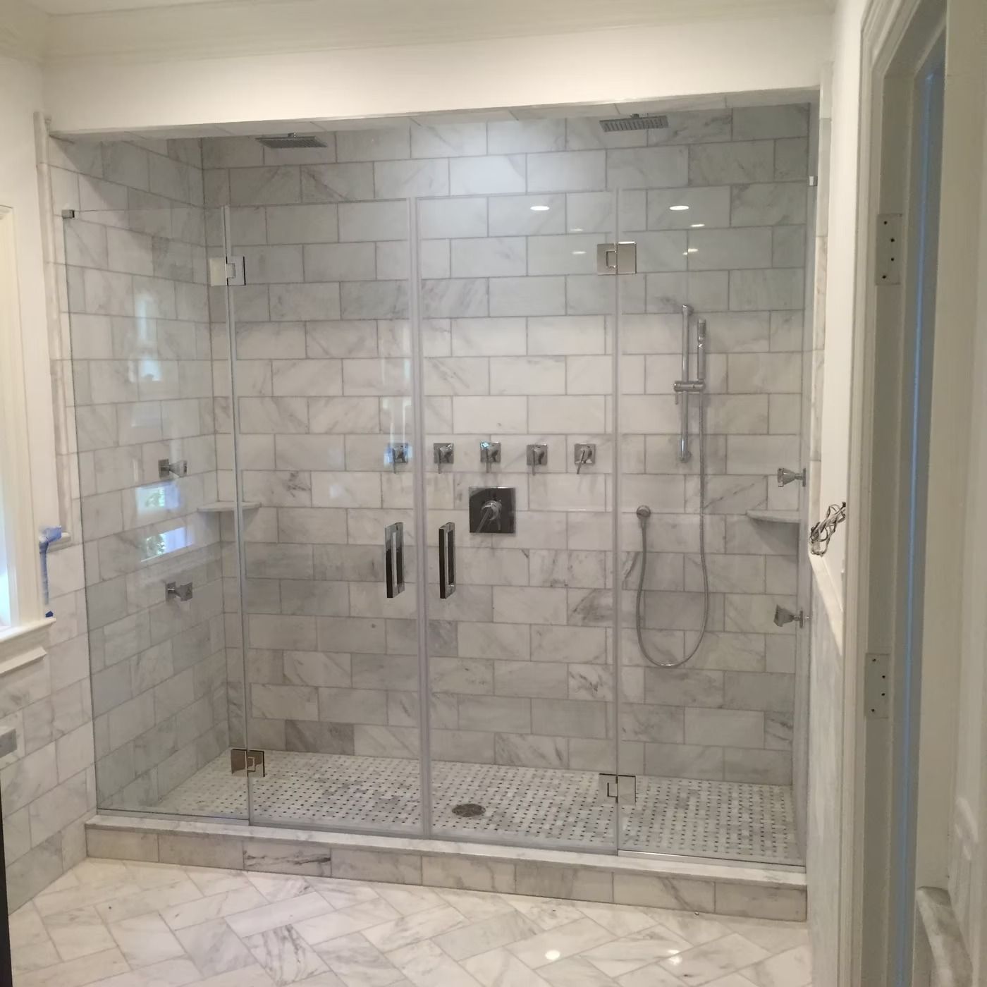 Modern glass walk-in shower with white subway tile and pebble floor in a bright bathroom