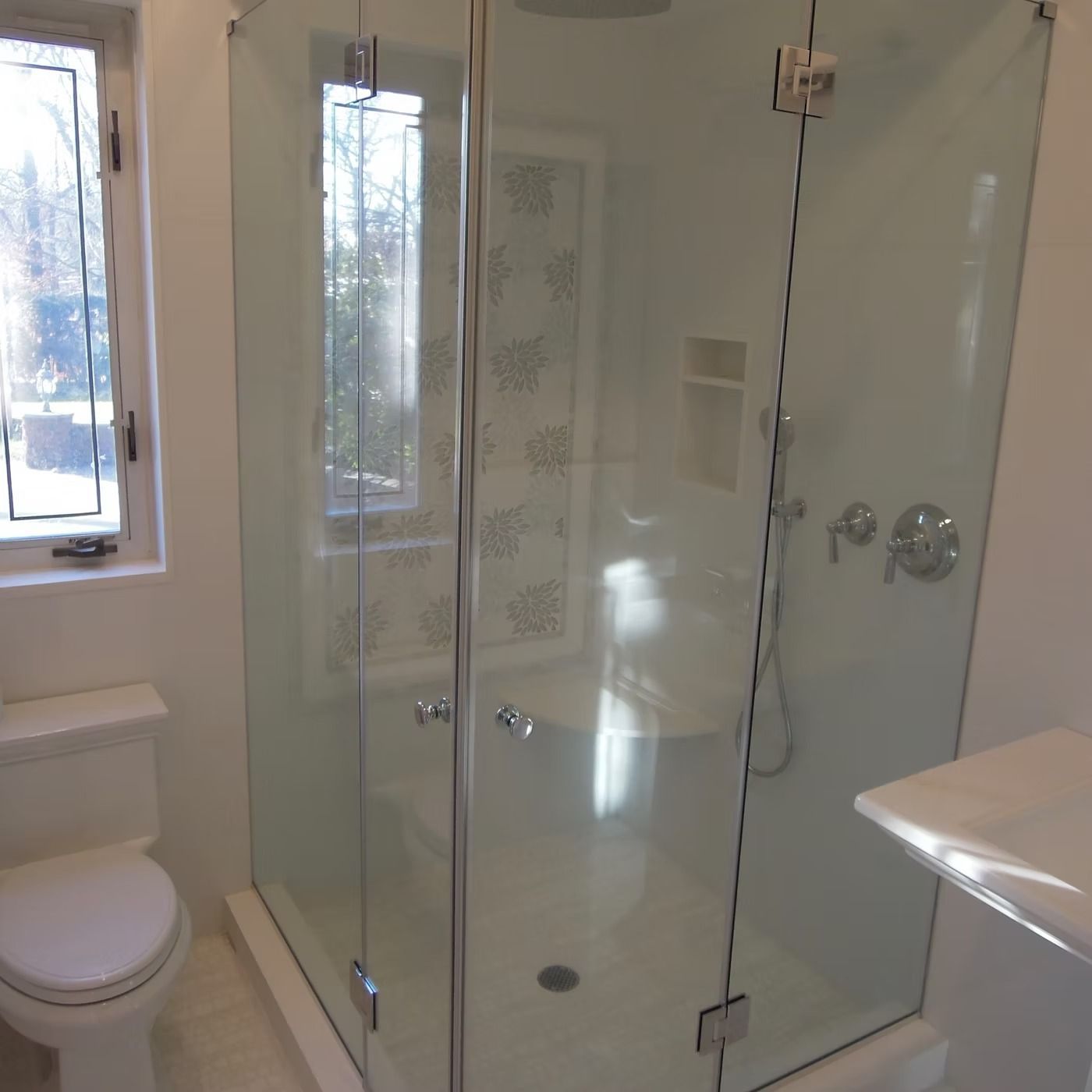 Modern bathroom with a glass walk-in shower, white toilet, and window light.