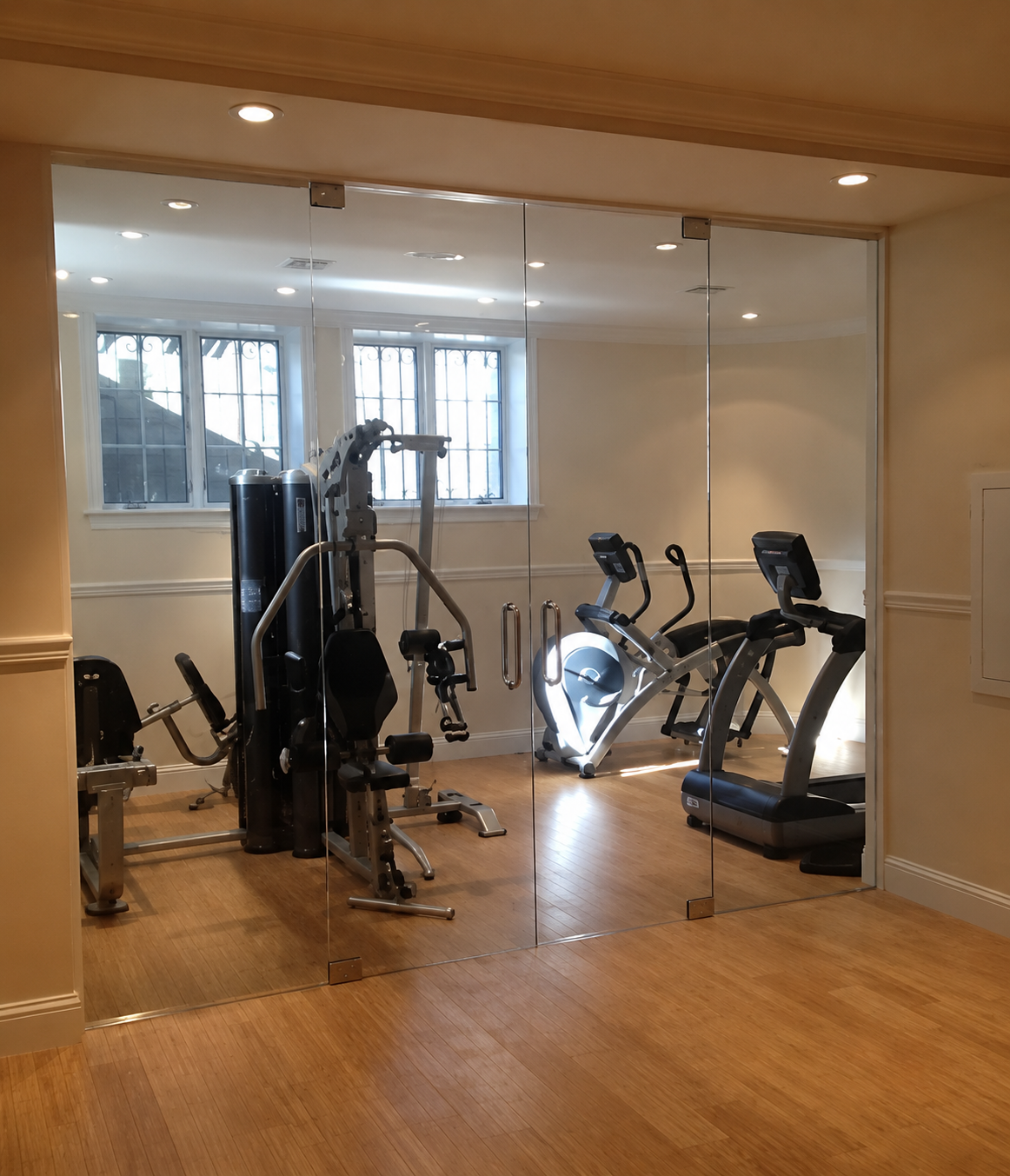 Gym with mirrored wall, wooden floor, and several cardio and weight machines.