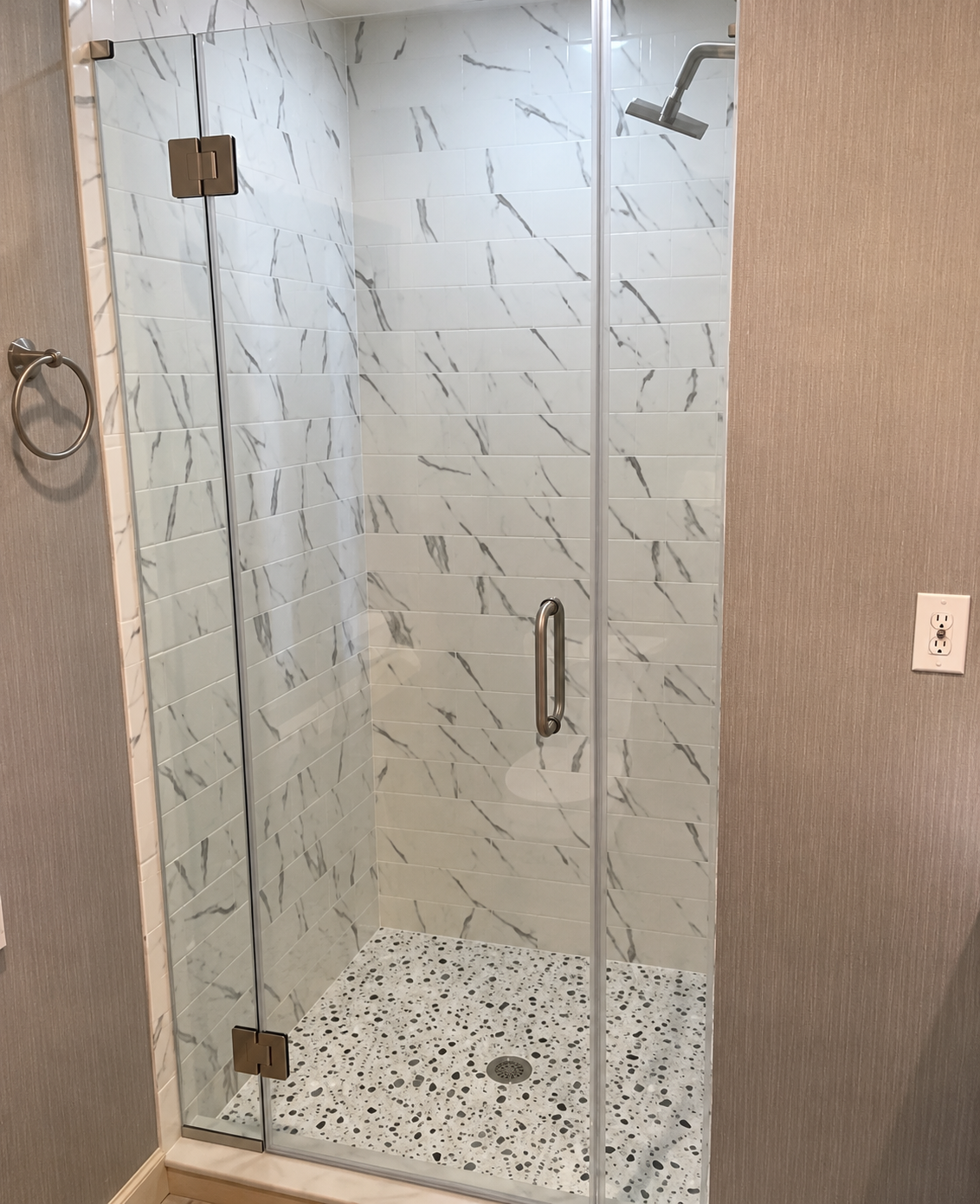 Glass shower enclosure with marble-look tile walls and speckled stone shower floor.