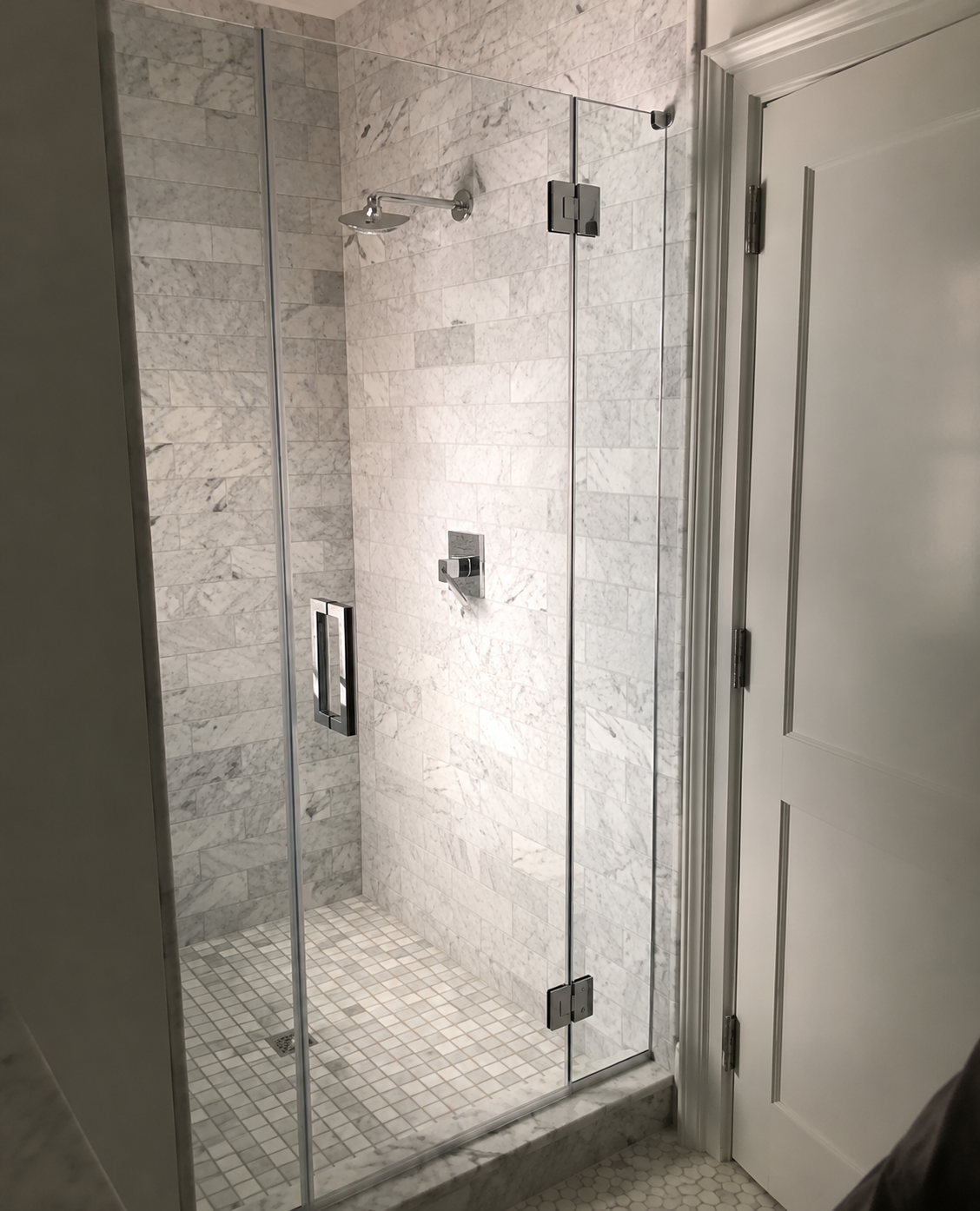 Modern tiled bathroom shower with frameless glass door and white entry door next to it
