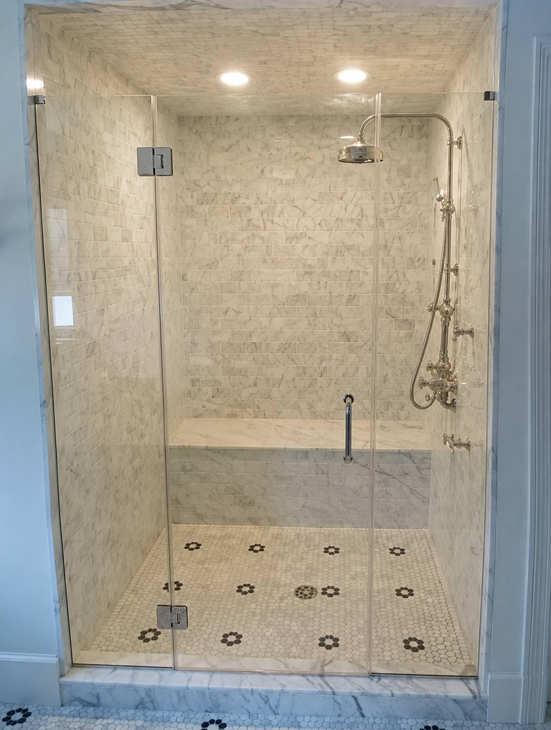 Glass walk-in shower with beige tile walls, patterned floor, and chrome shower fixtures.