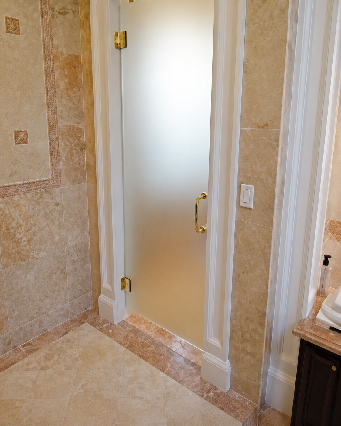 Frosted glass shower door with gold handle in a beige tiled bathroom