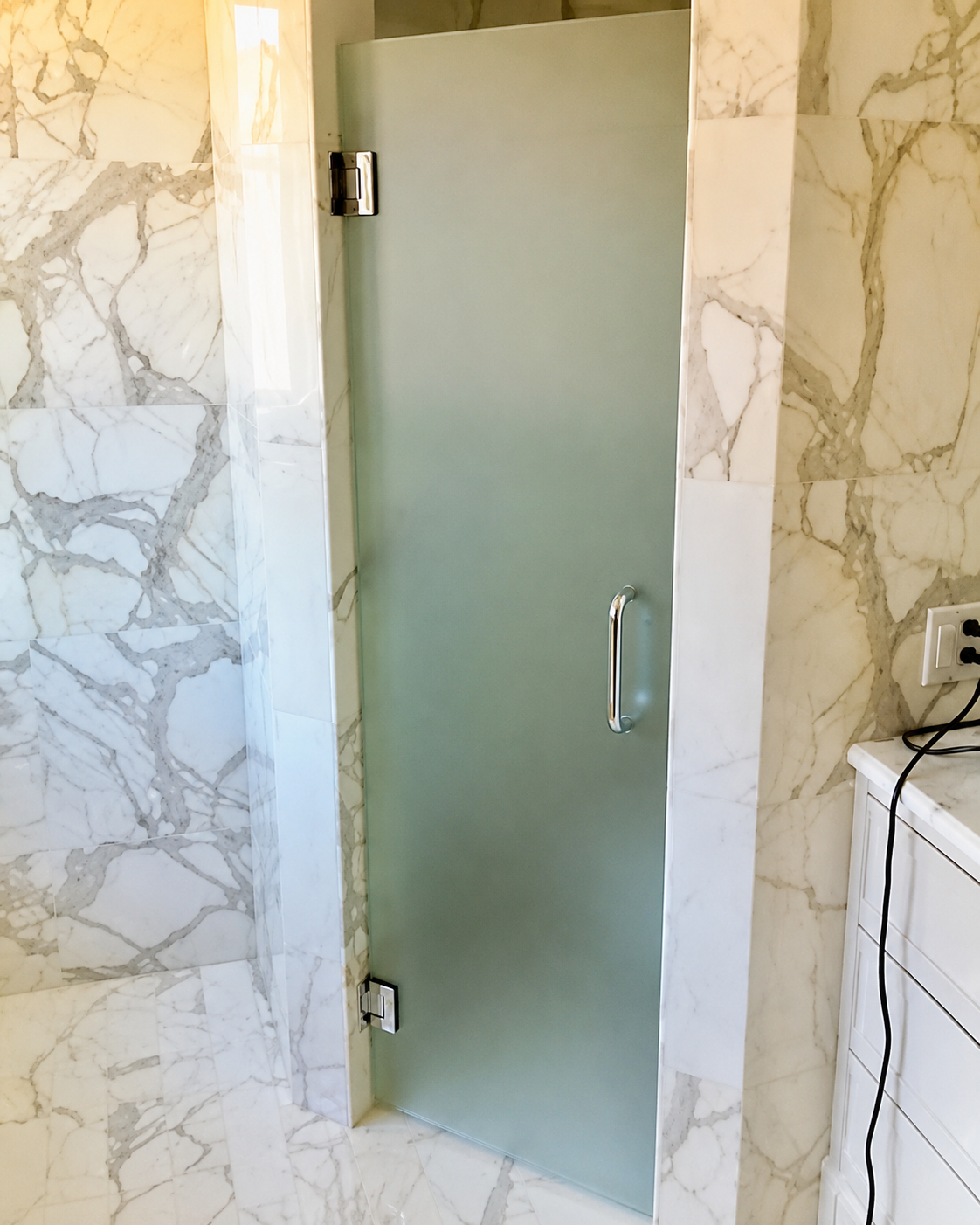 Frosted glass shower door with metal handle in a tiled bathroom