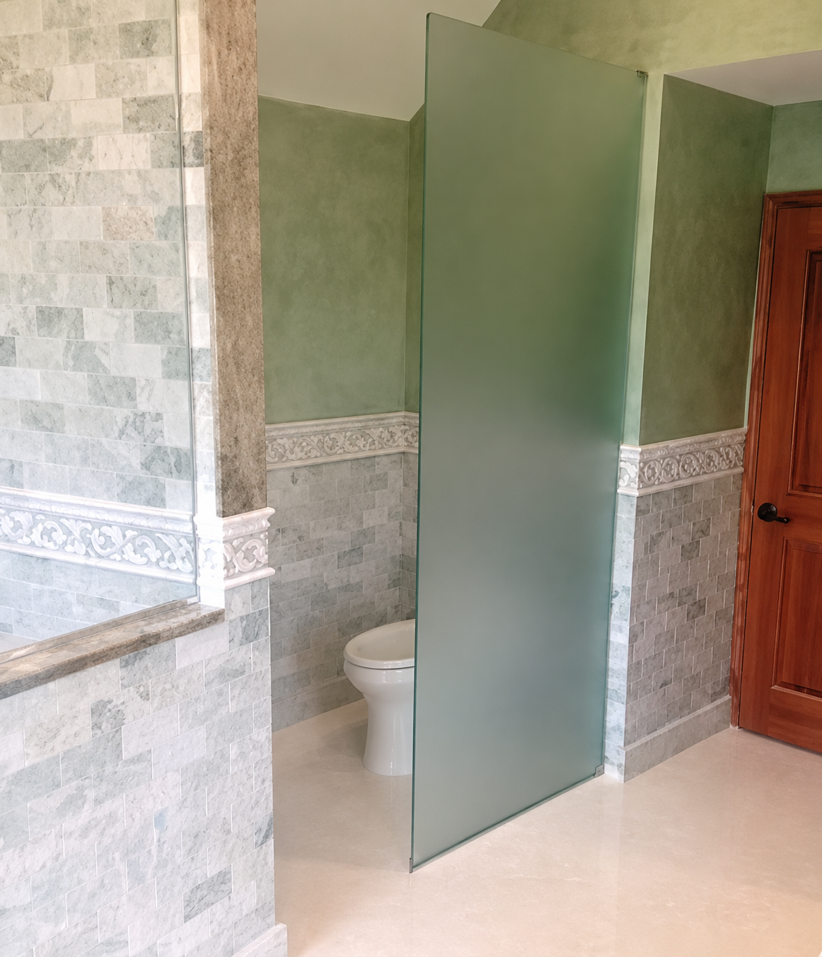 Modern bathroom with green walls, tiled half-wall, frosted glass shower panel, and wooden door