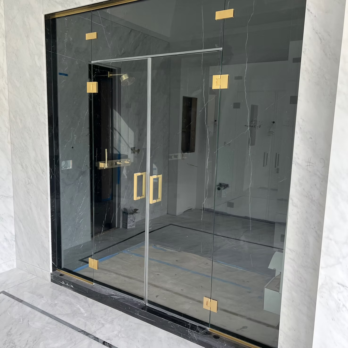 Modern glass shower enclosure with black frame and gold handles in a tiled bathroom alcove
