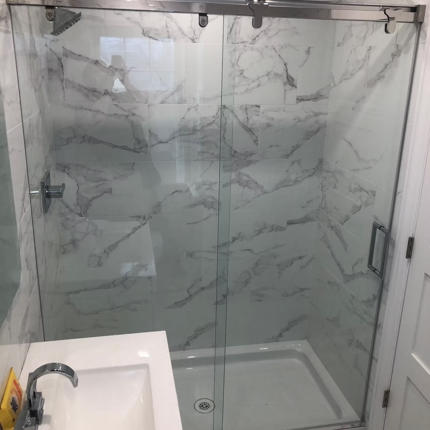 Small bathroom with marble-tiled shower, glass door, and a white sink in the foreground.