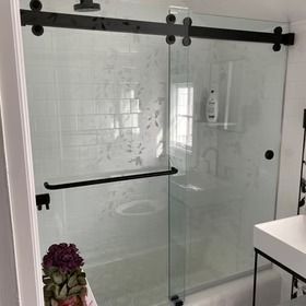 Glass shower enclosure with black hardware in a bright white bathroom
