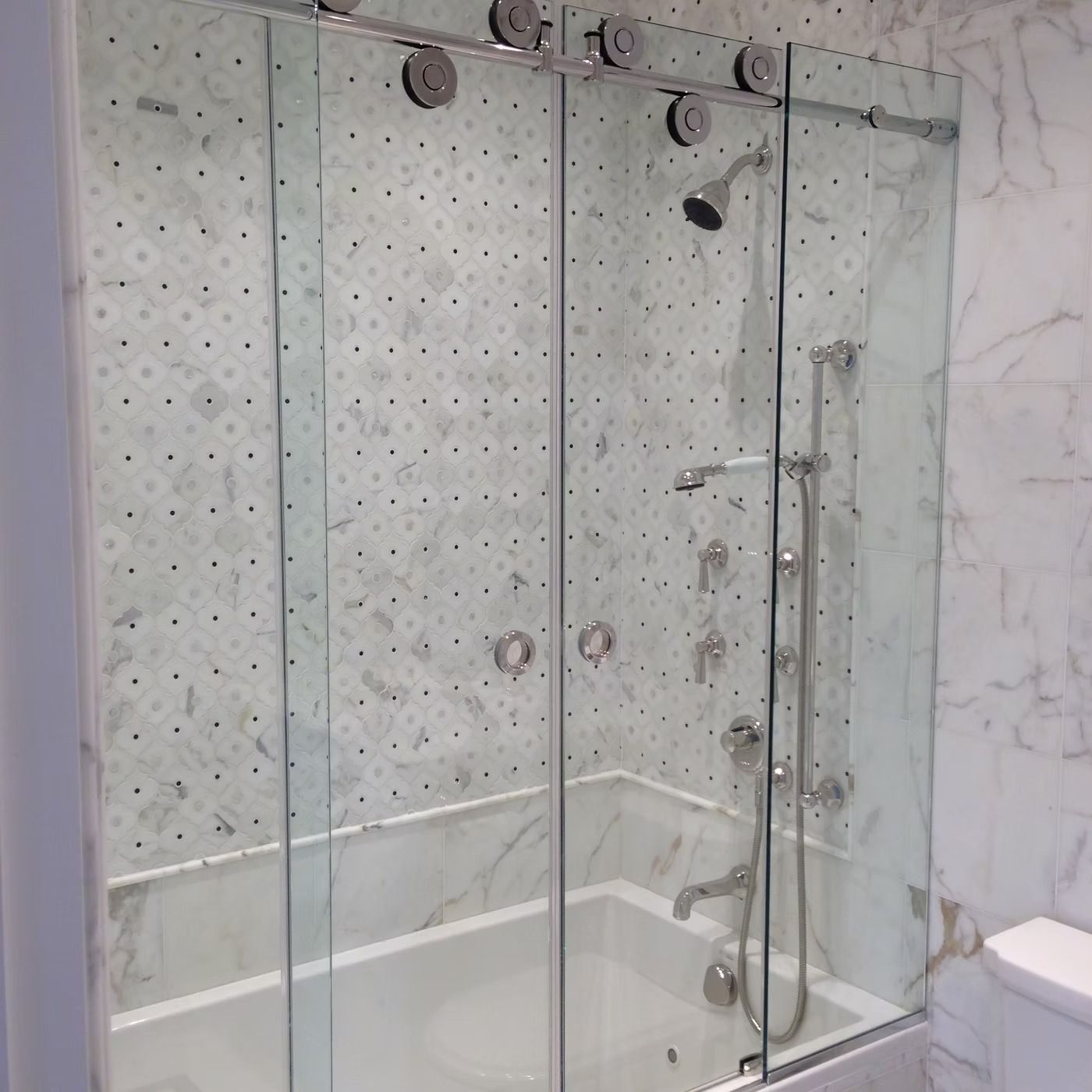 Glass walk-in shower with gray tile walls, chrome fixtures, and a white tub edge