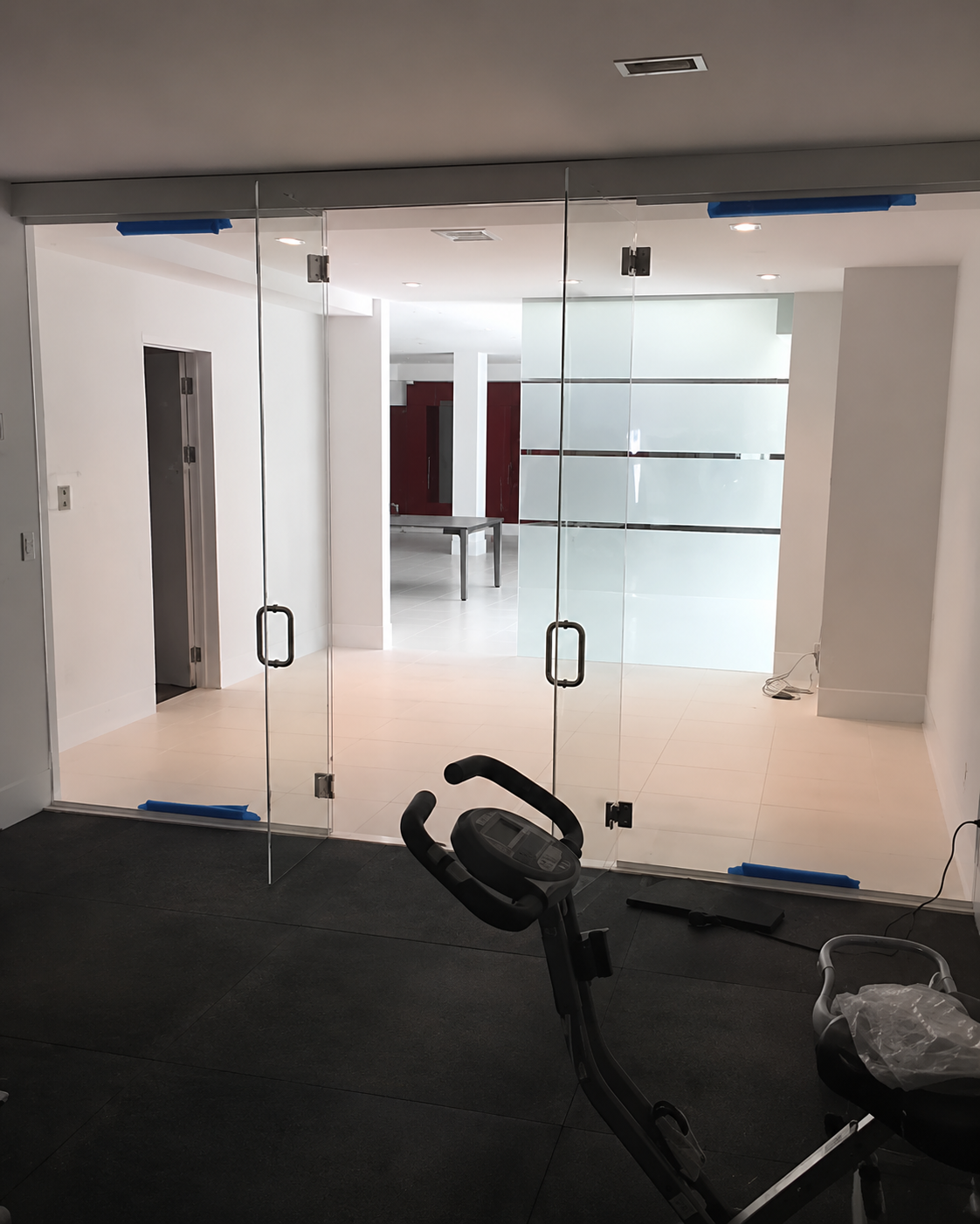 Glass lobby doors with white walls and a stationary bike in the foreground.