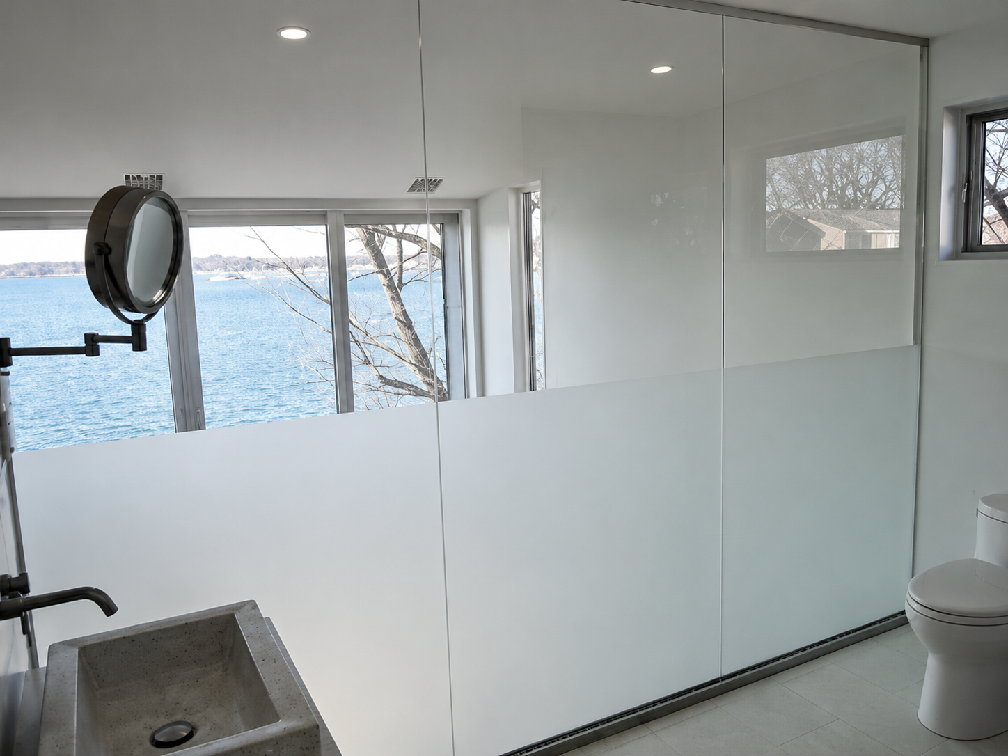 Modern bathroom with frosted glass wall, sink, toilet, and view of water outside