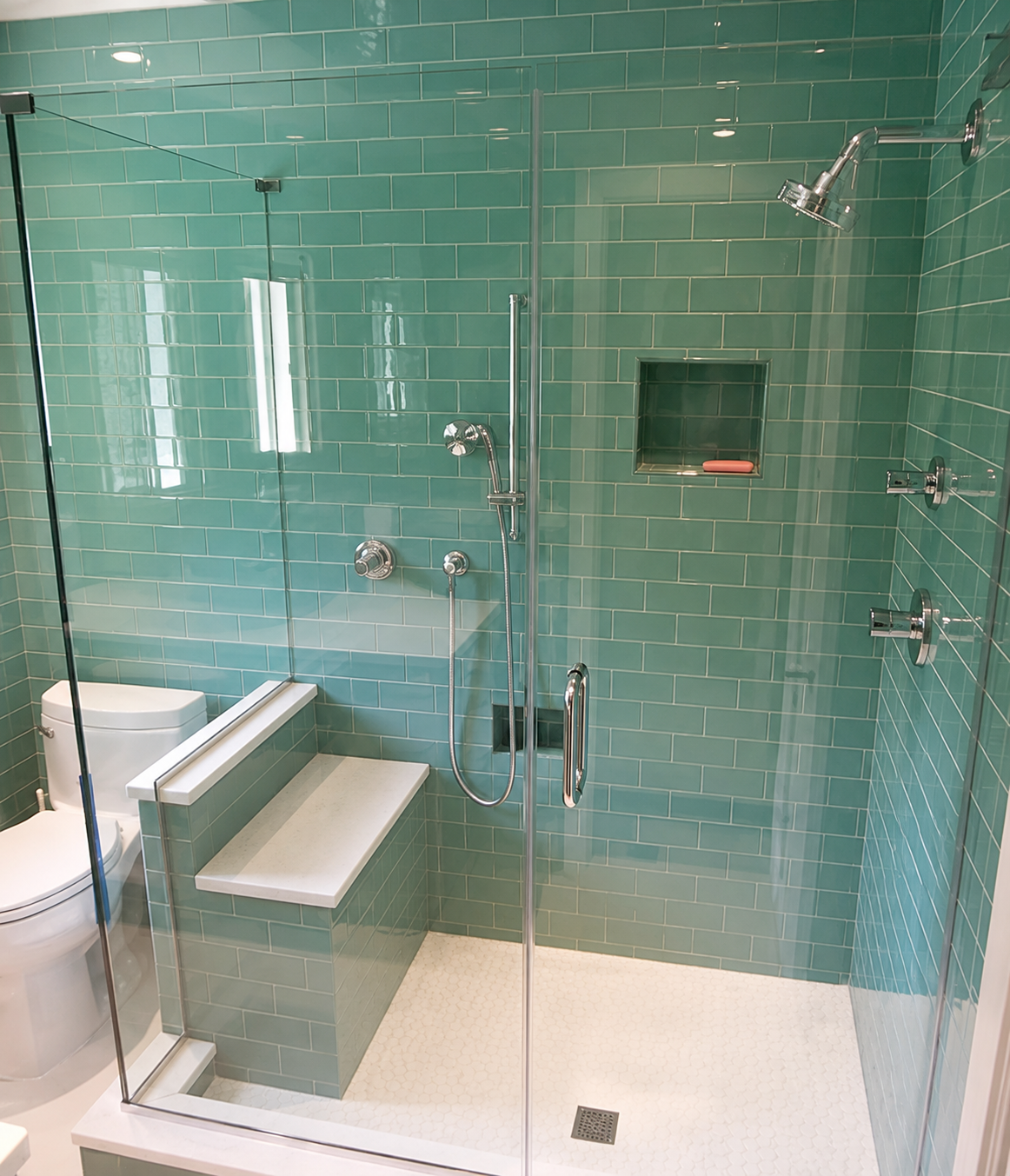 Accessible glass shower with teal tile walls, built-in bench, grab bars, and shelf niche.