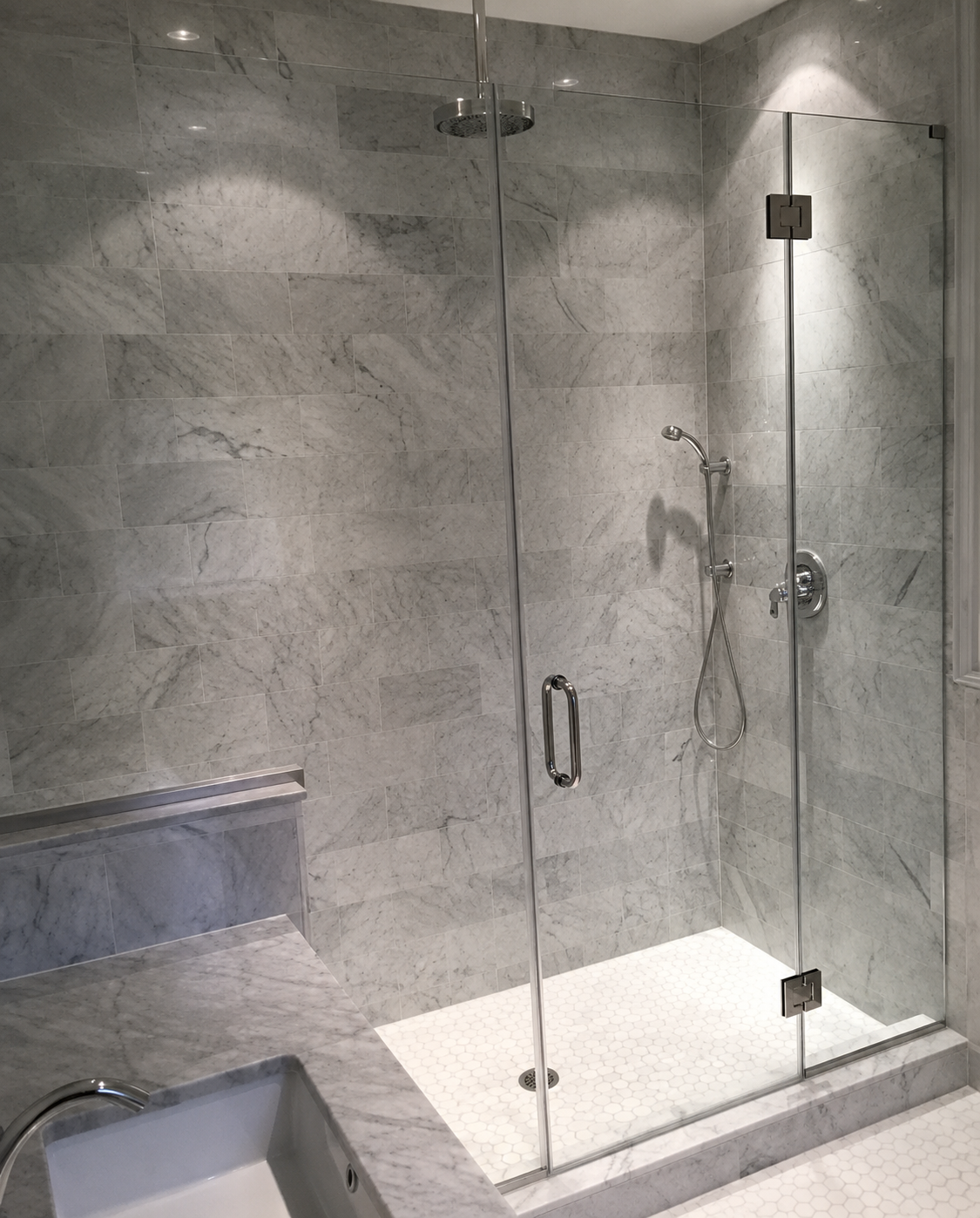 Glass-enclosed marble shower with built-in bench and chrome fixtures in a bathroom