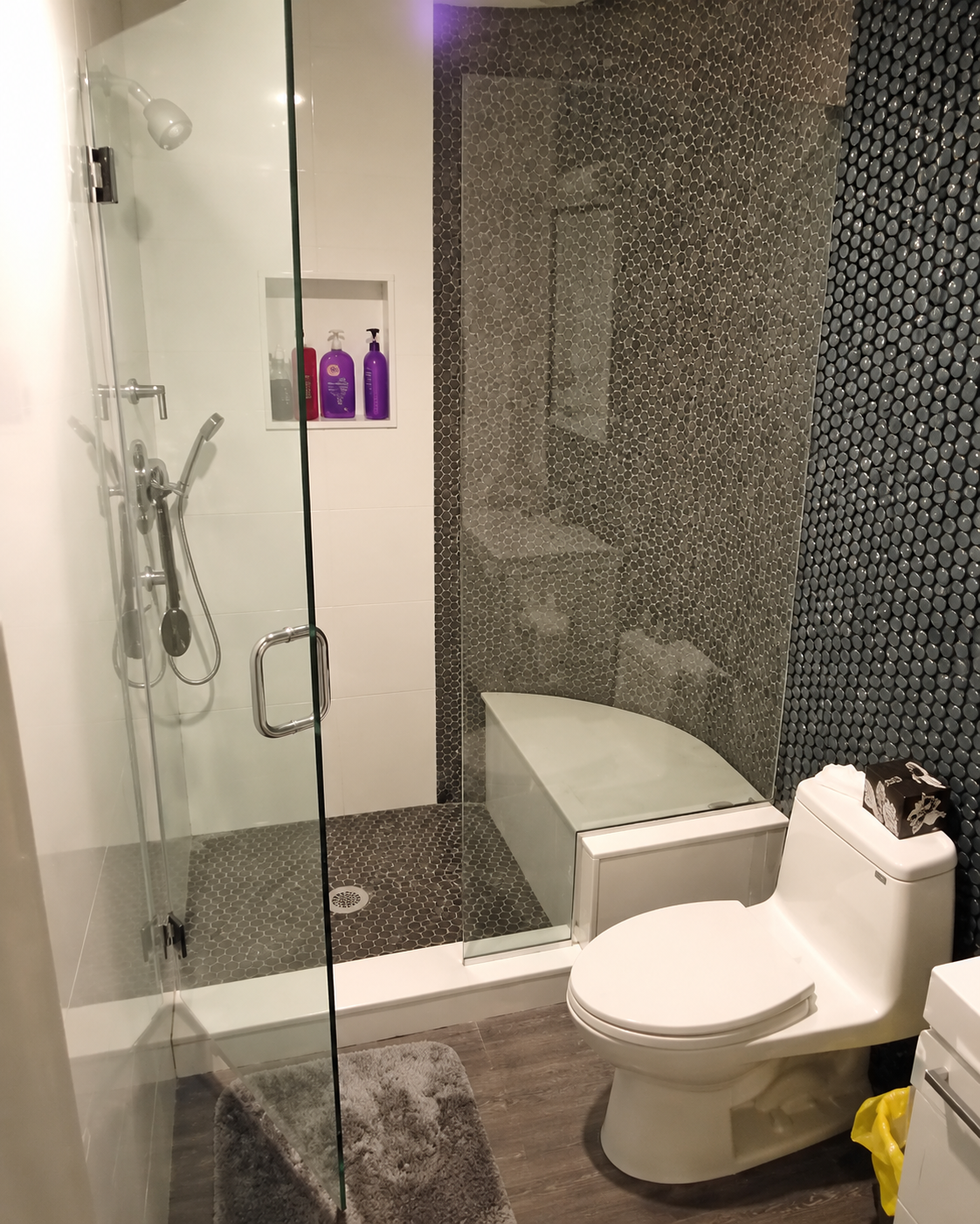 Modern bathroom with glass shower, toilet, sink, and dark textured wall tile