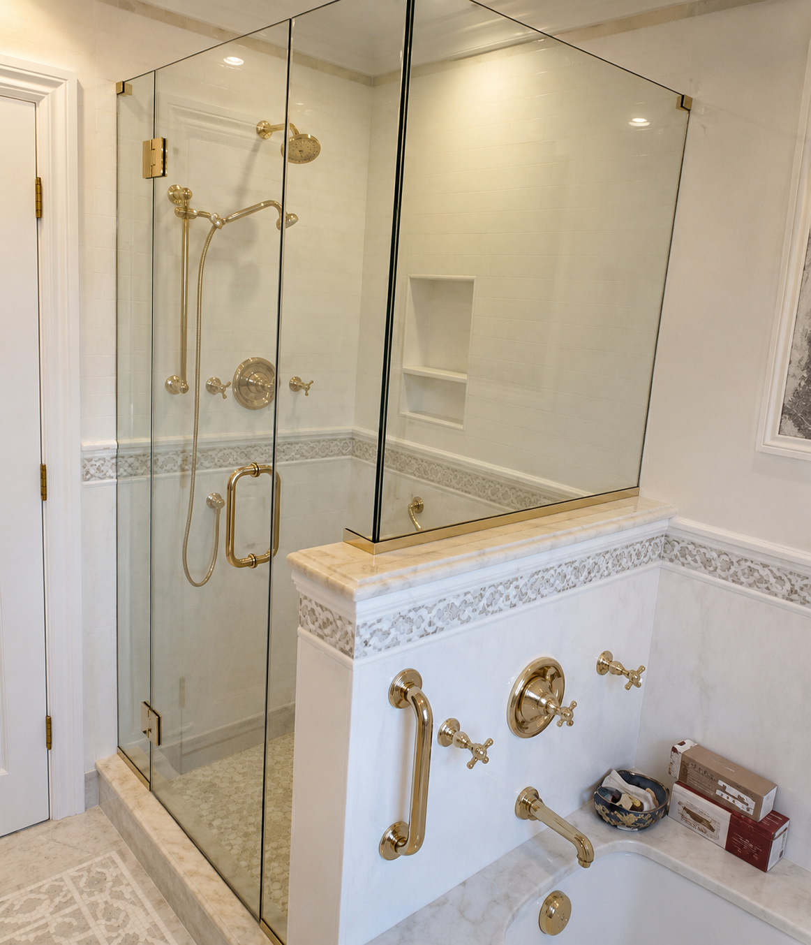 Glass shower enclosure and white marble bathroom with gold fixtures and wall mirror.