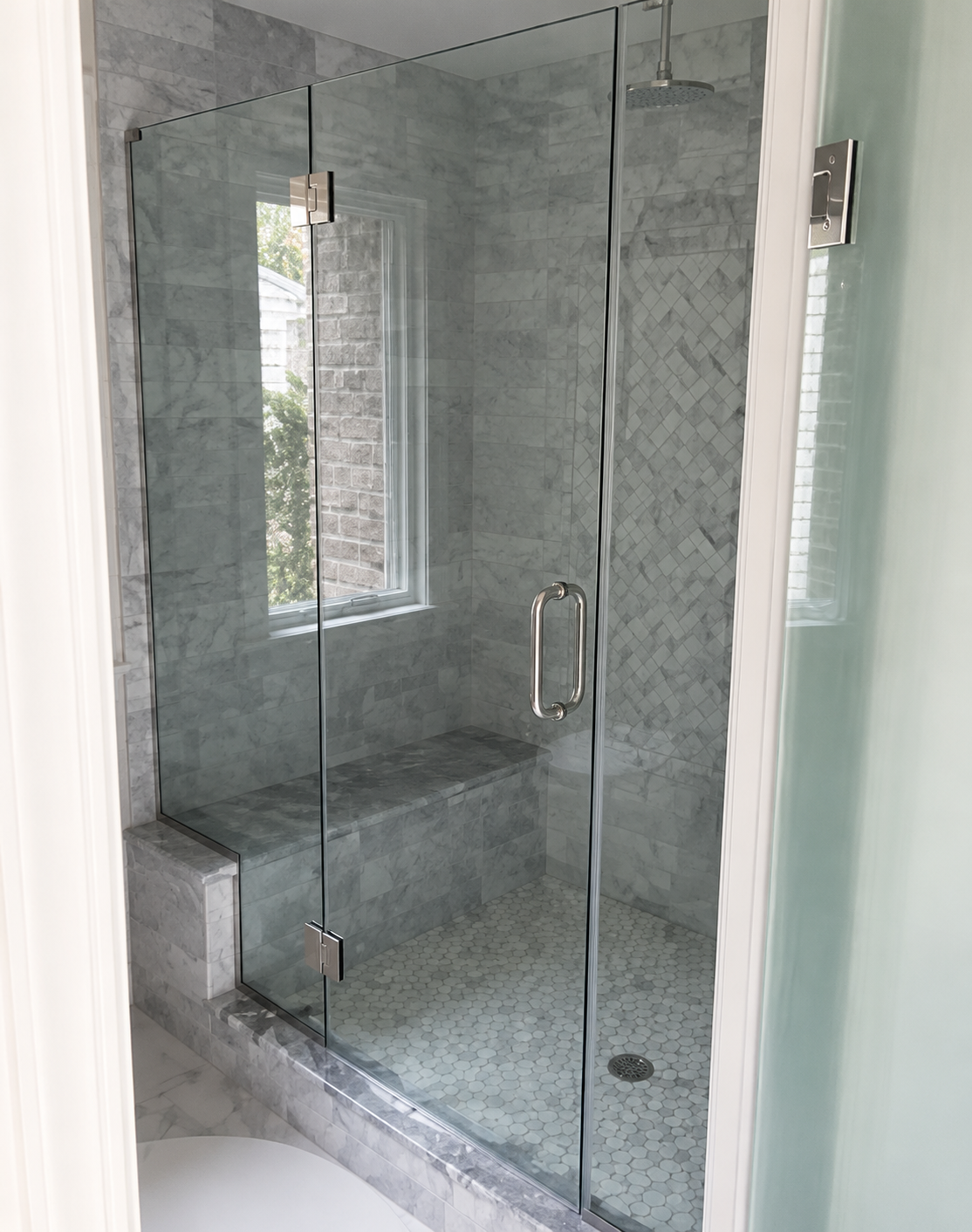 Glass walk-in shower with gray tile, built-in bench, and chrome fixtures