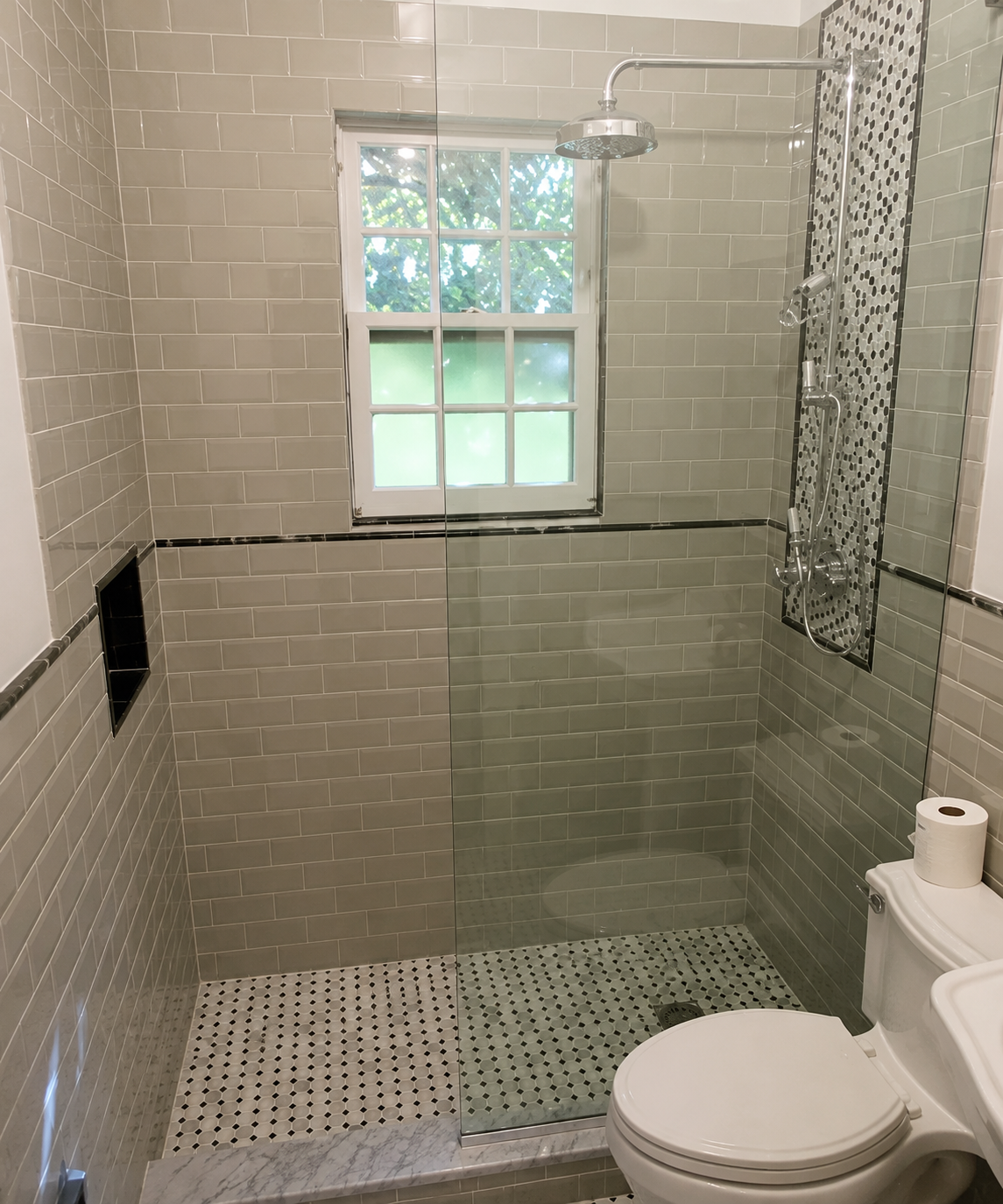 Accessible tiled shower with bench, grab bar, window, and toilet paper holder beside a toilet