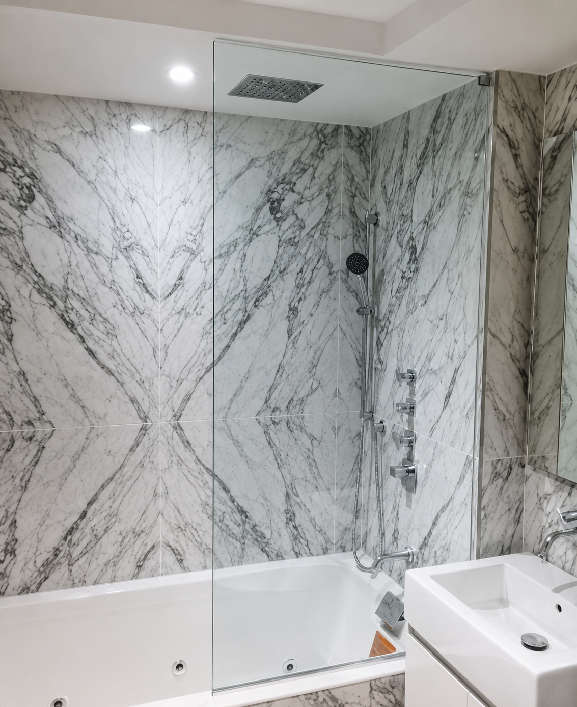 Marble-tiled bathroom with a bathtub, showerhead, and vanity sink beneath a wall mirror.