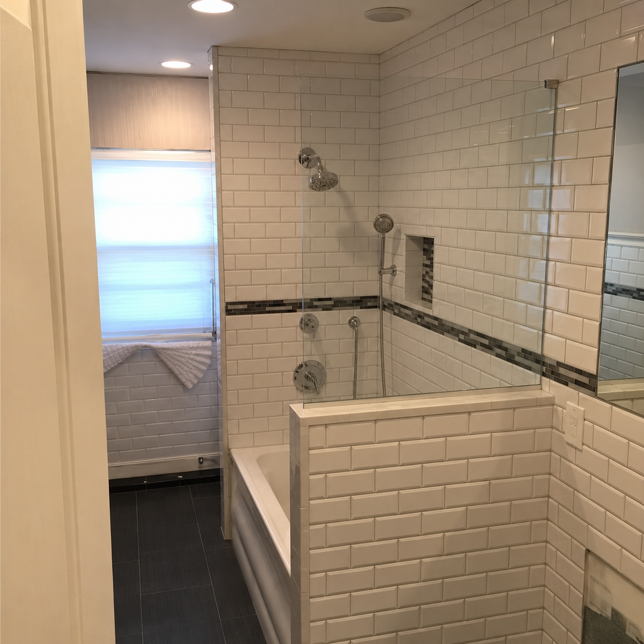 Small white-tiled bathroom with a bathtub, showerhead, and frosted window.