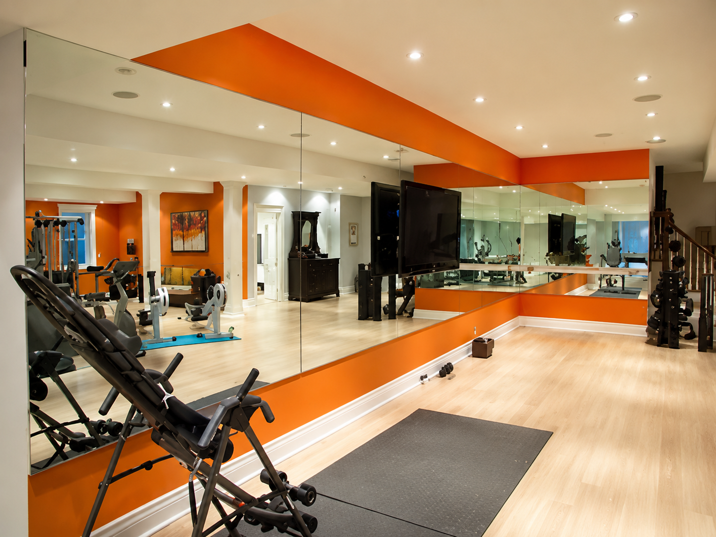 Modern gym studio with mirrors, orange accents, workout equipment, and wooden floors