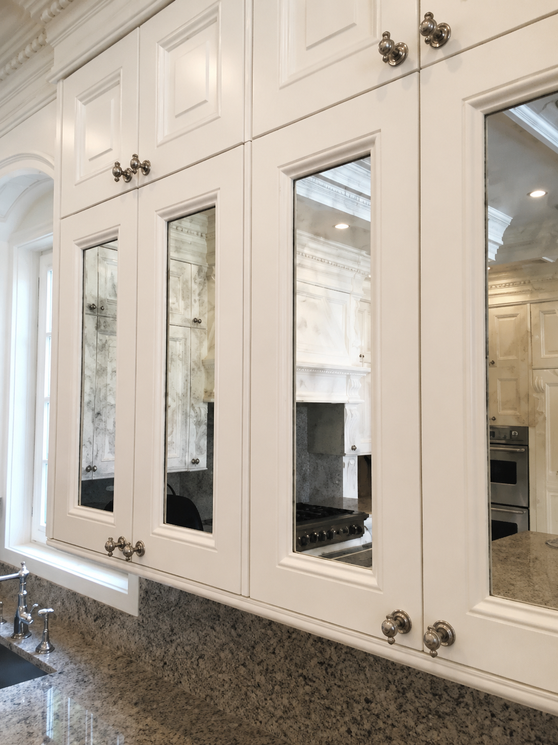 White kitchen cabinets with mirrored glass panels above a speckled granite countertop