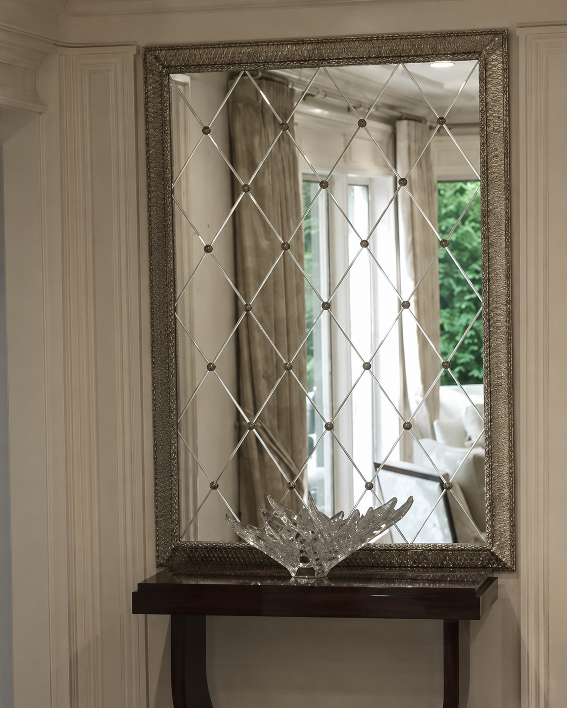 Decorative diamond-pattern mirror above a dark console table in a bright hallway