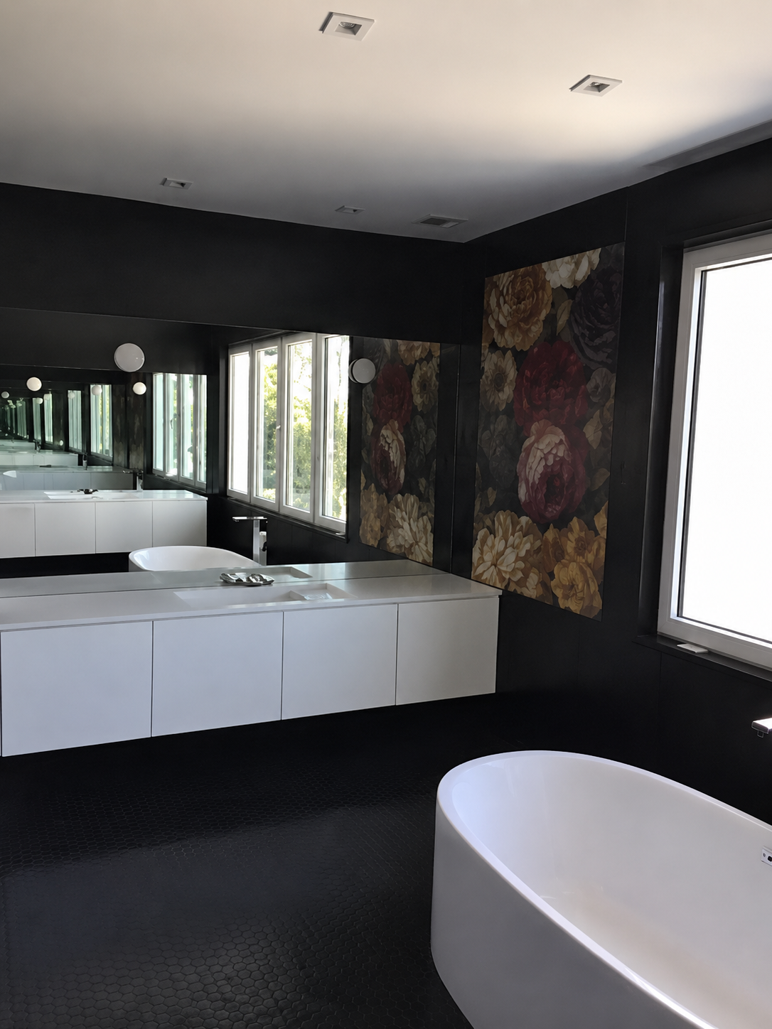 Modern black bathroom with a large mirror, white vanity, and freestanding tub by tall windows