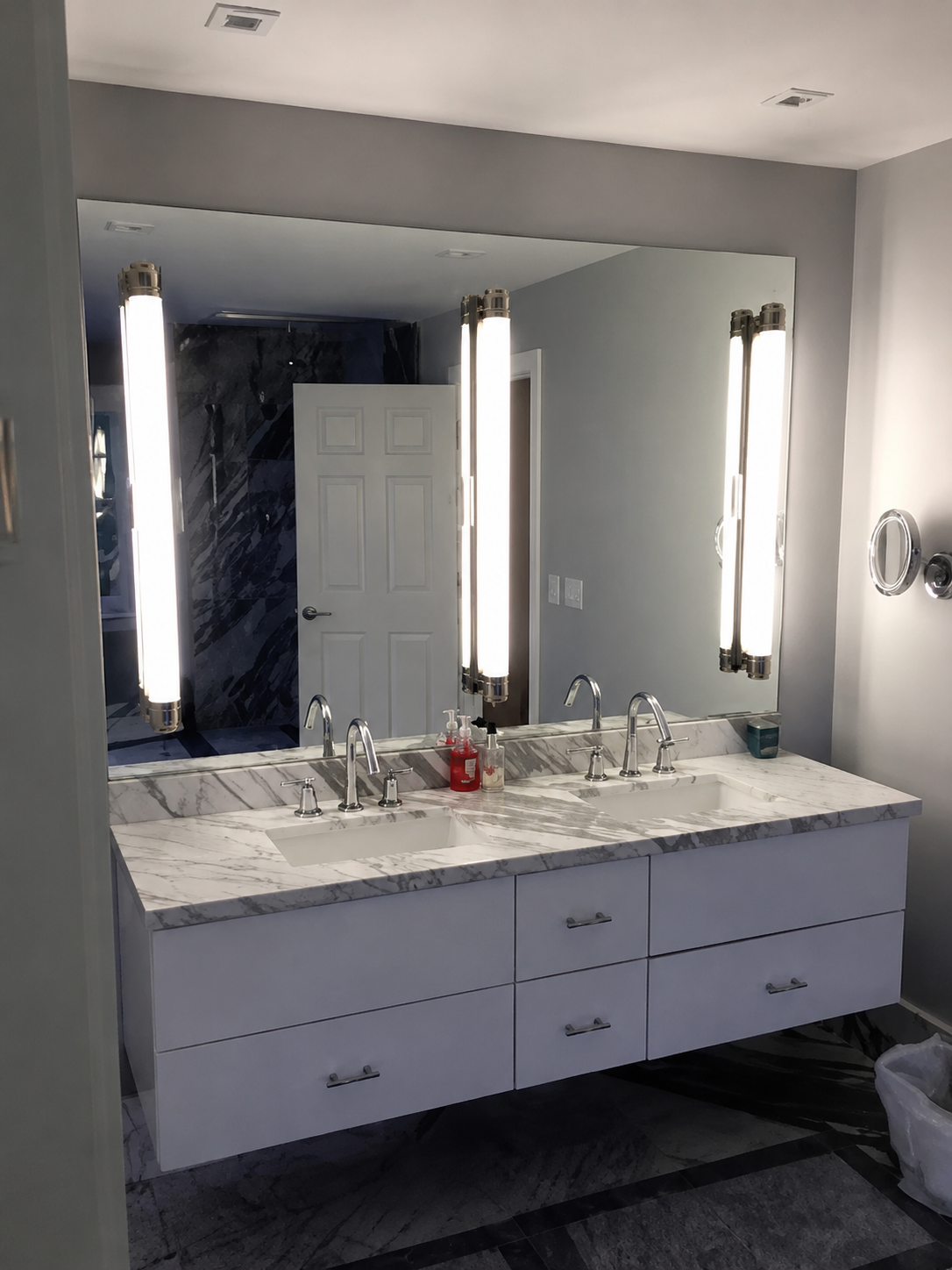 Modern bathroom vanity with dual sinks, large mirror, and bright vertical light fixtures