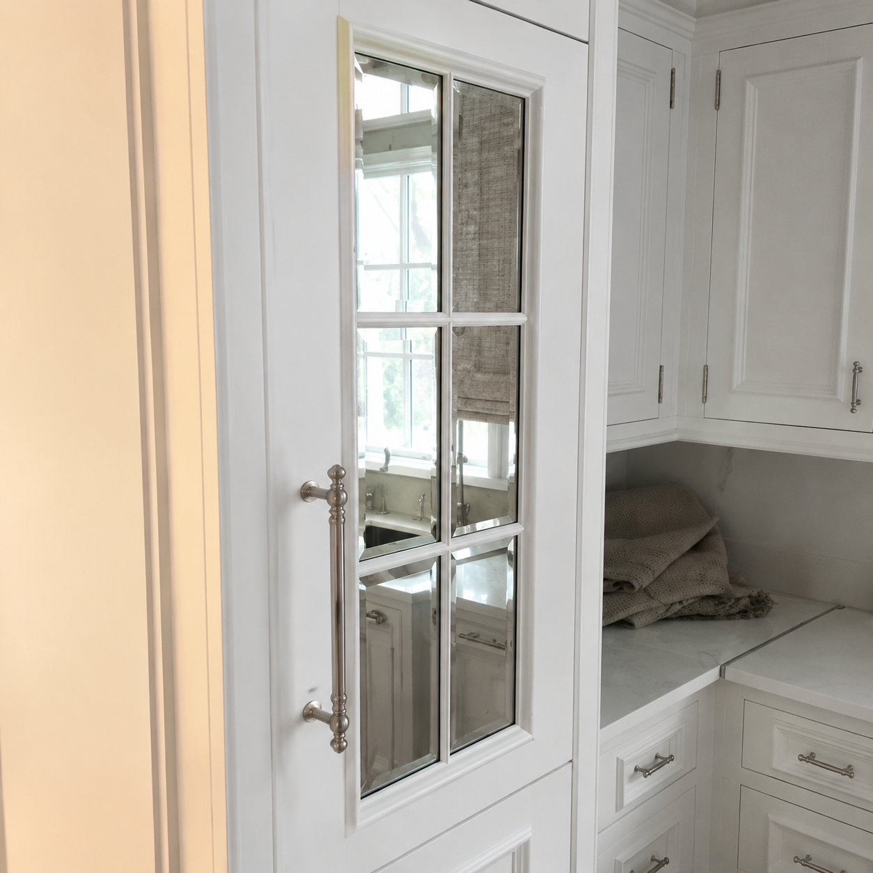 White built-in cabinets and a glass-paneled door beside a cushioned window seat in a bright room