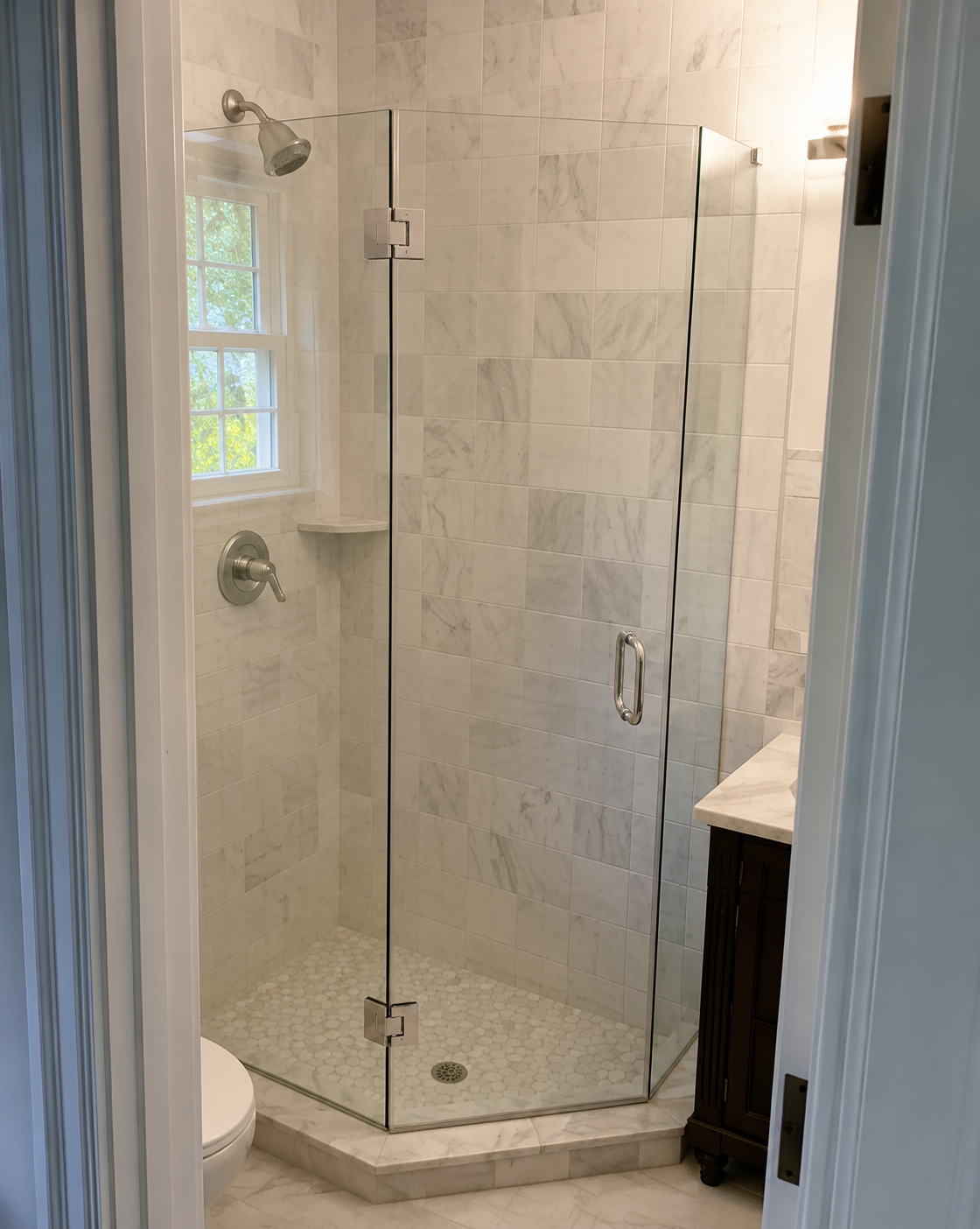 Glass corner shower with white tile walls, chrome fixtures, and a small vanity beside it.