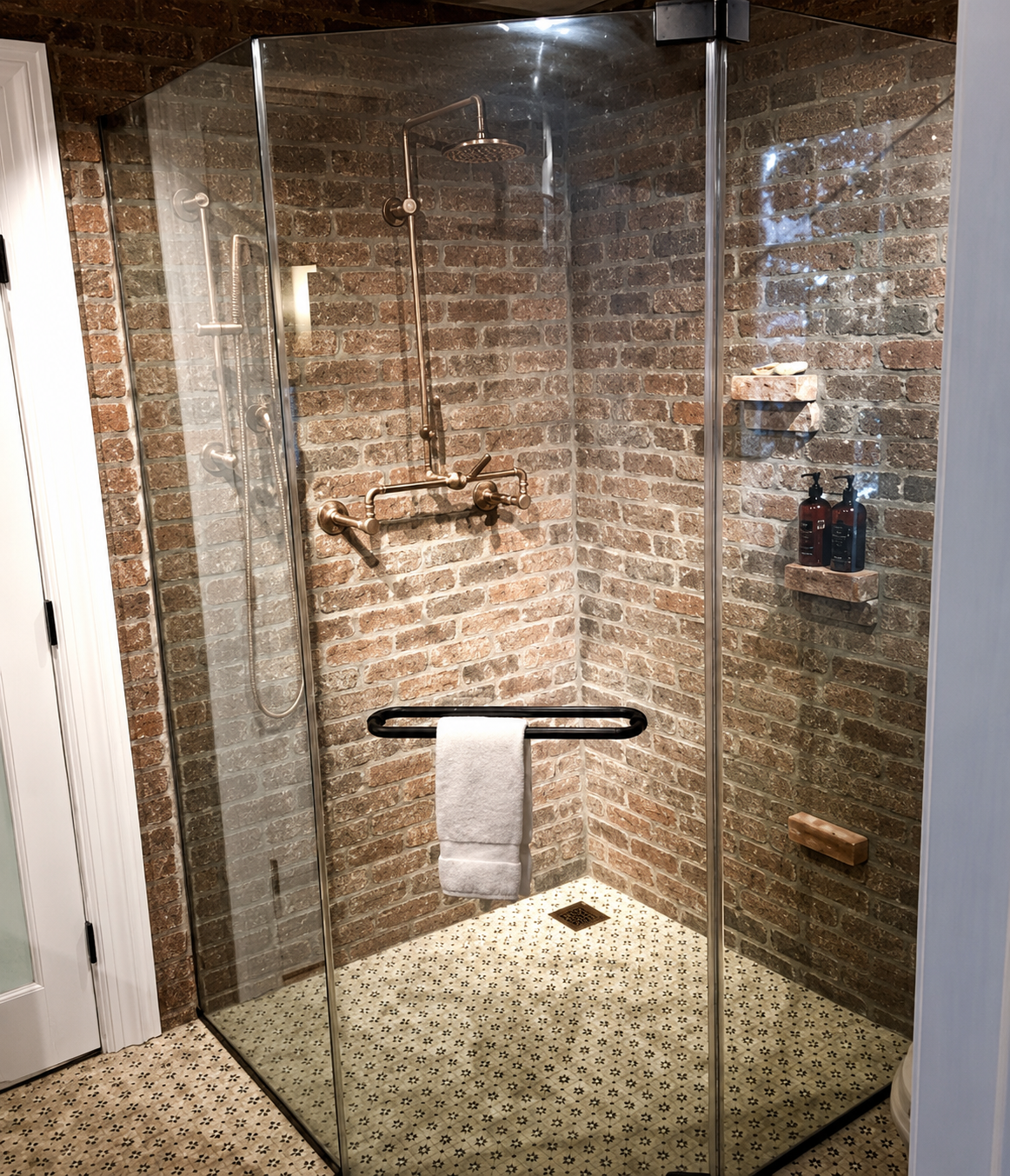 Glass-enclosed walk-in shower with brick walls and a pebble-tile floor, featuring a wall-mounted grab bar.