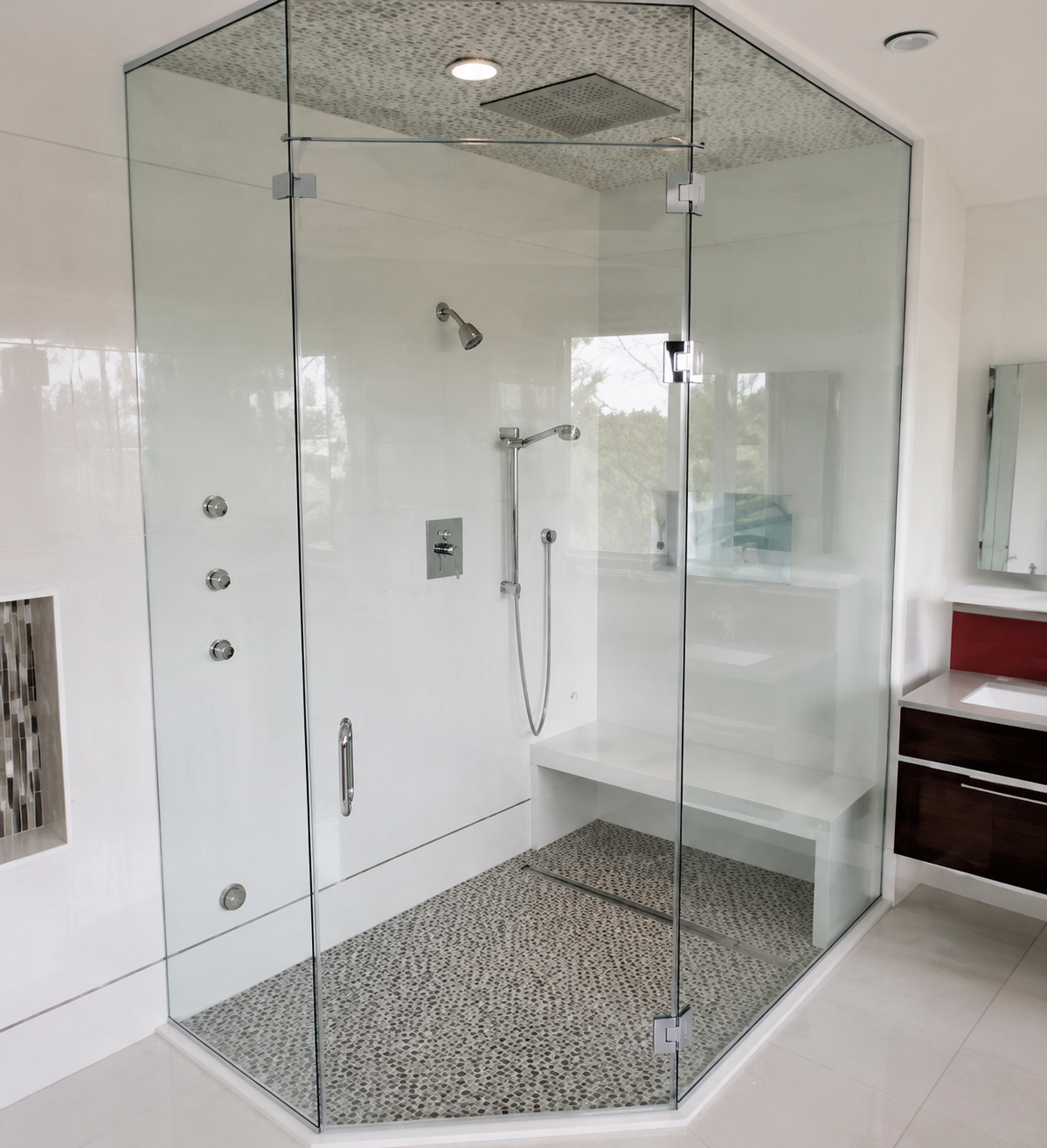 Modern glass walk-in shower with pebble floor and chrome fixtures in a bright bathroom