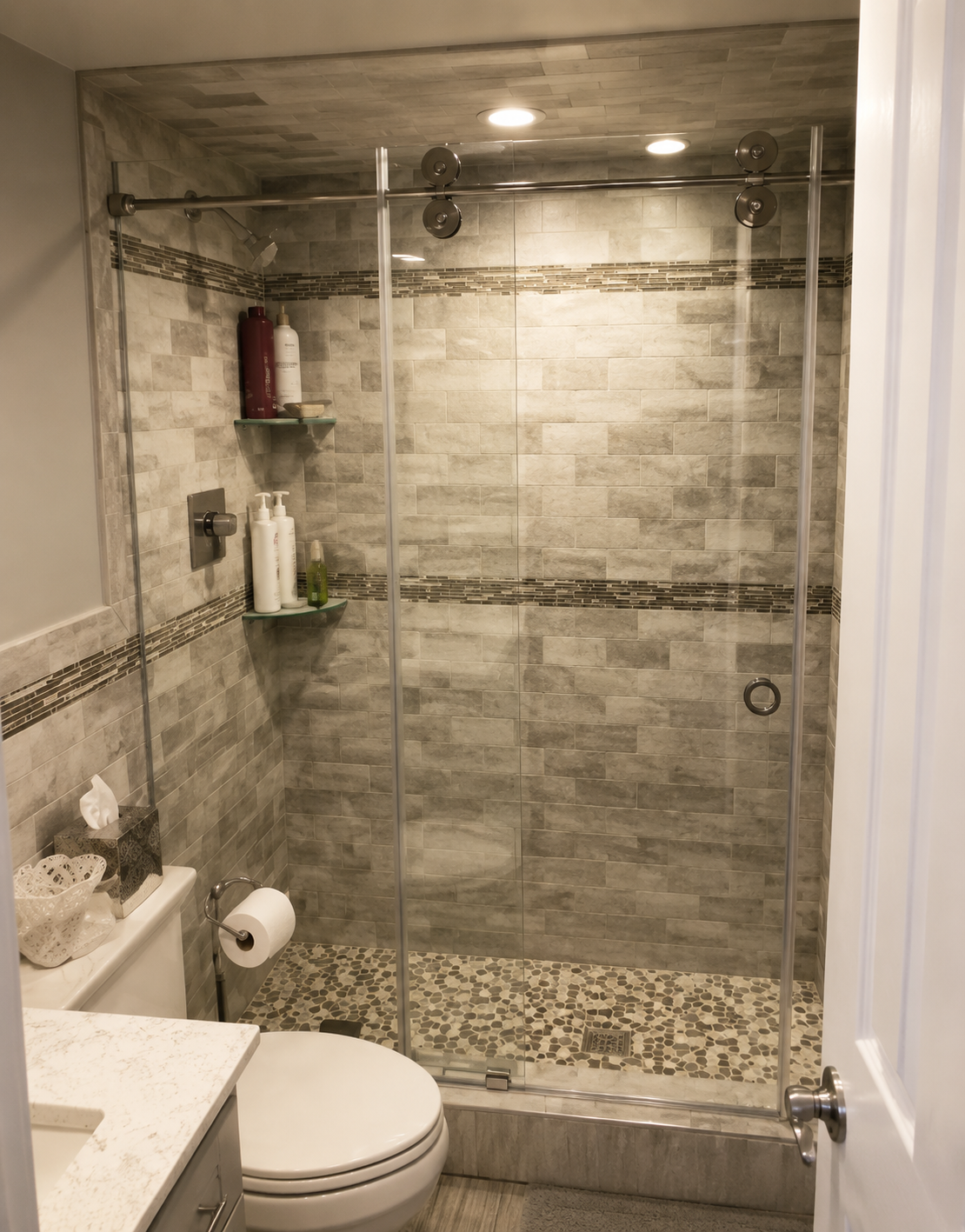Tiled walk-in shower with glass doors beside a toilet in a small bathroom