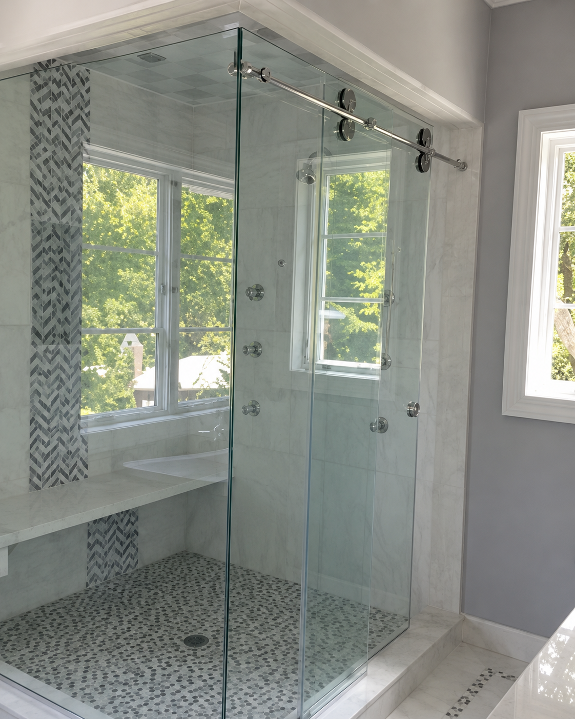 Glass walk-in shower with rain head, pebble tile floor, and white vanity in a bright bathroom