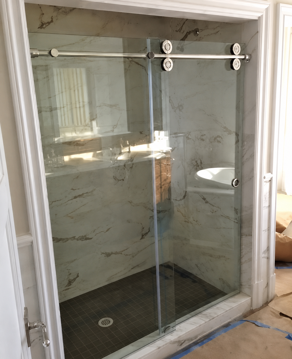 Modern glass shower enclosure with marble walls and a dark tile floor