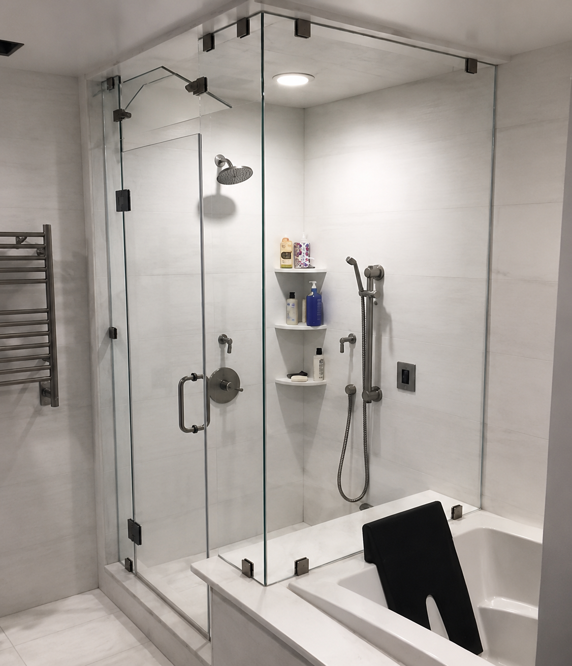 Modern bathroom with glass shower, white tile, and a black towel draped over the tub.