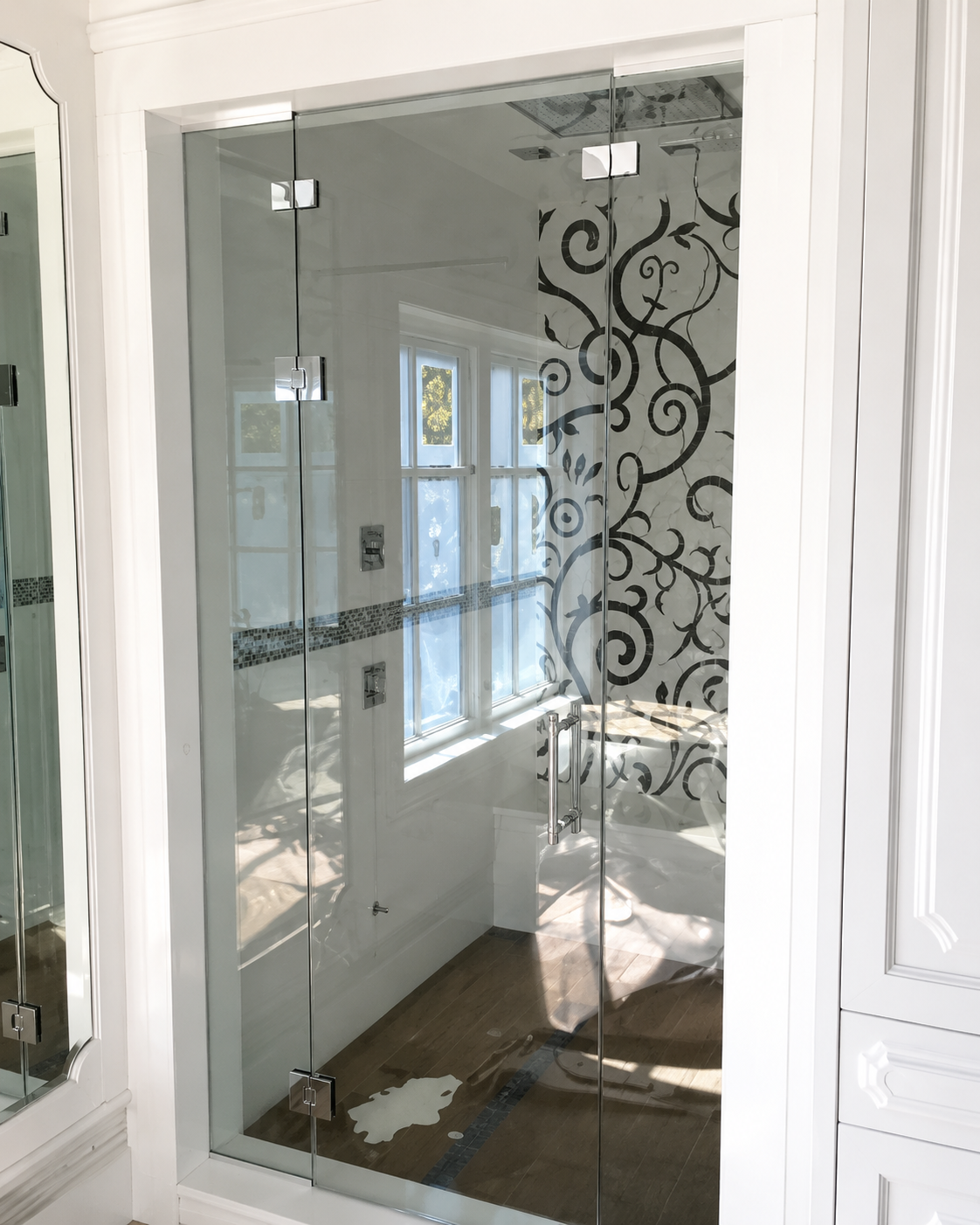 Glass bathroom shower enclosure with white frame and decorative black swirl pattern on the right panel.