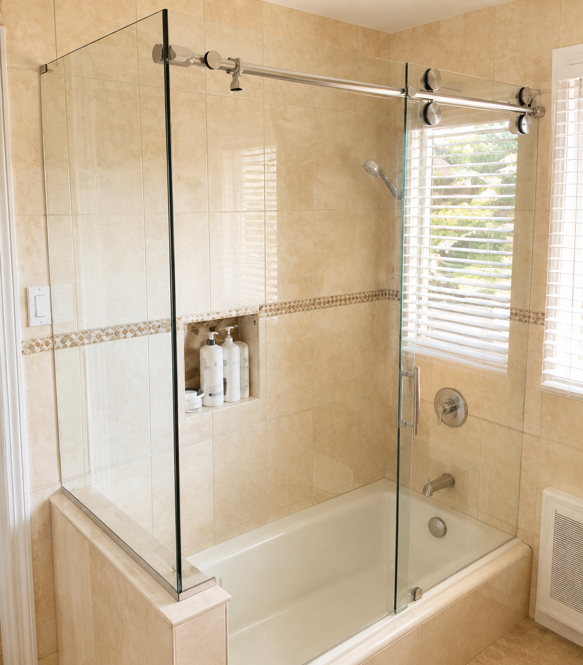 Glass-enclosed bathtub shower with beige tile, built-in shelf, and window blinds in a bathroom