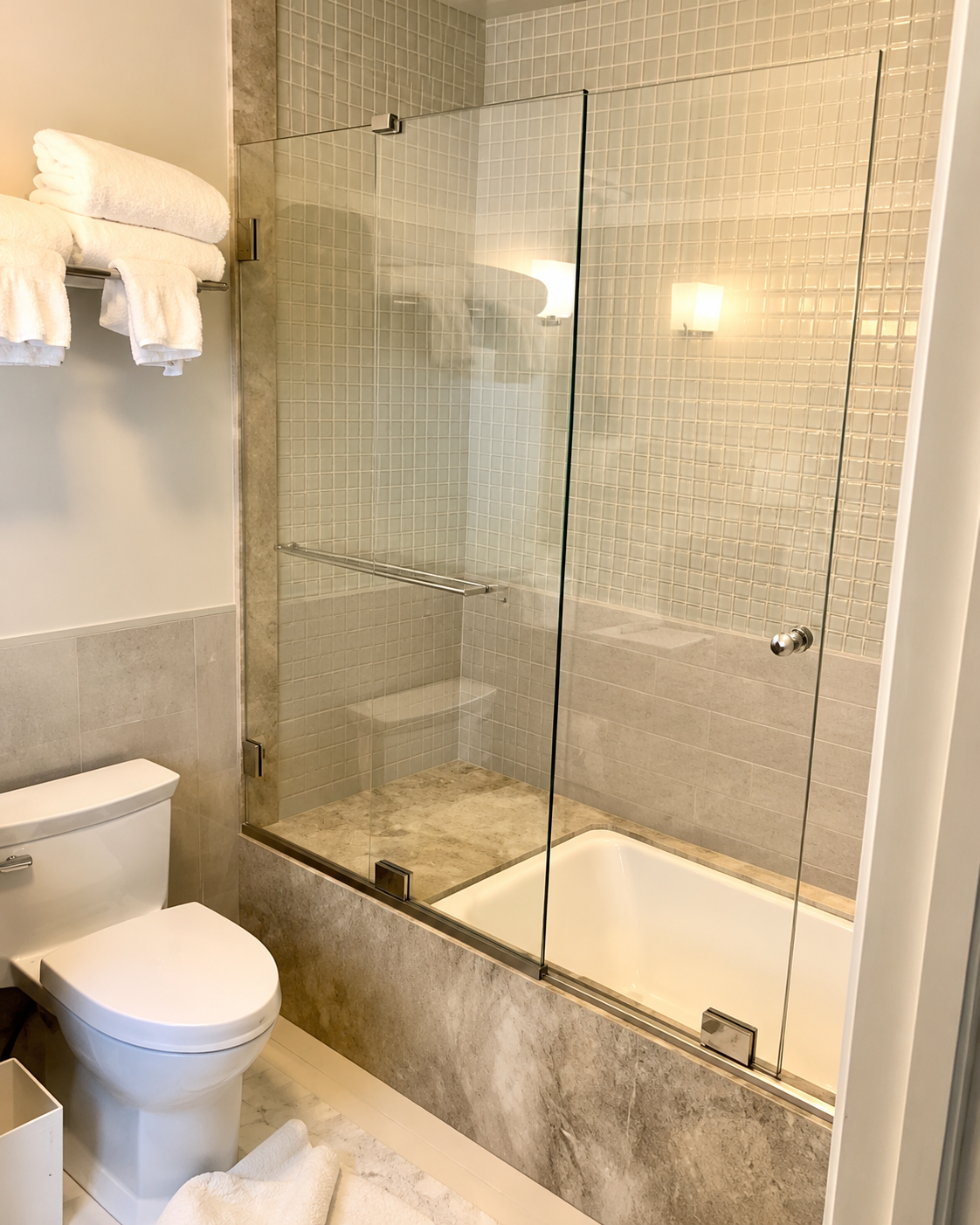 Bathroom with a toilet, glass-enclosed bathtub, and beige tiled walls.