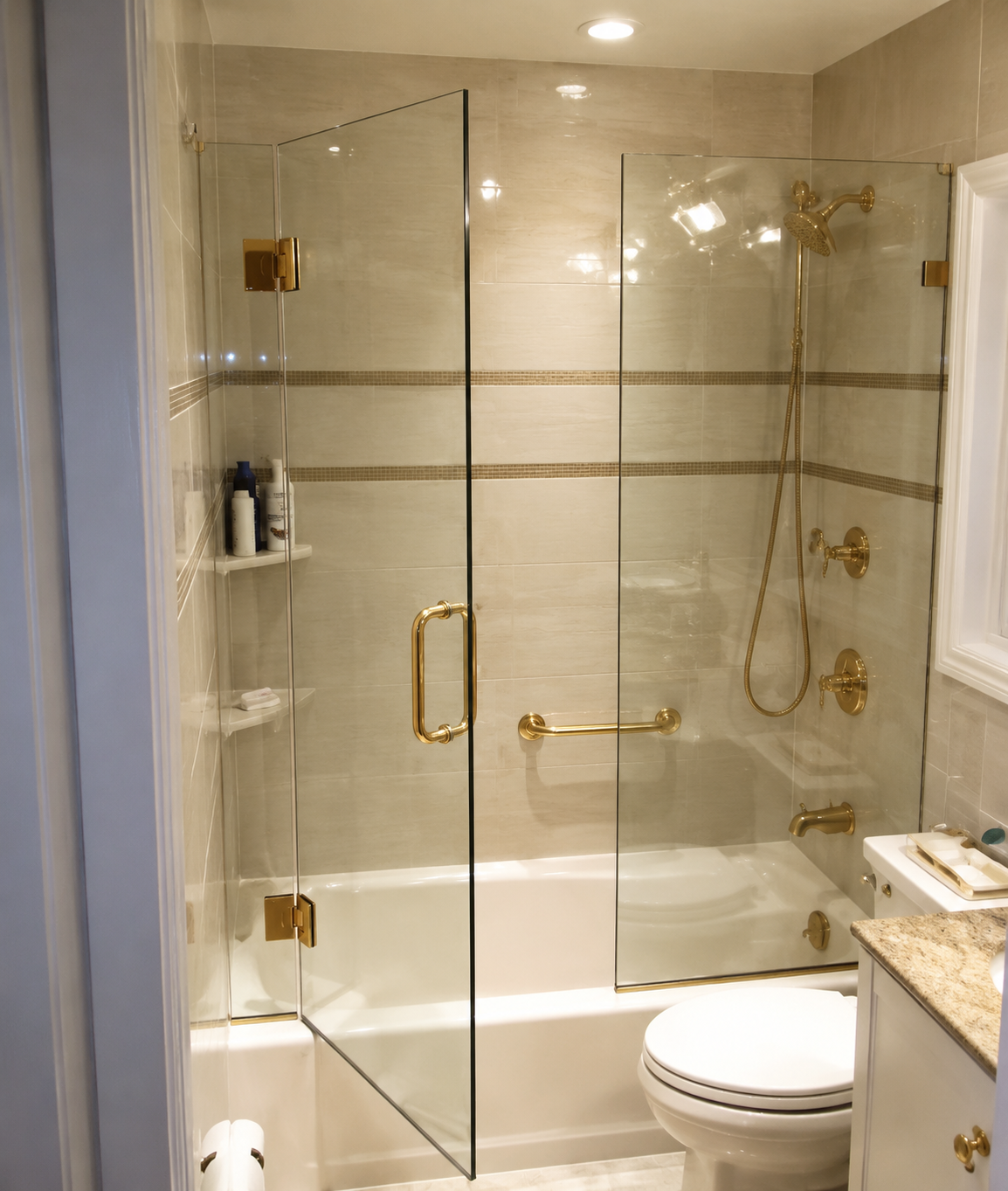 Modern beige-tiled bathroom with glass shower doors, bathtub, toilet, and granite vanity.