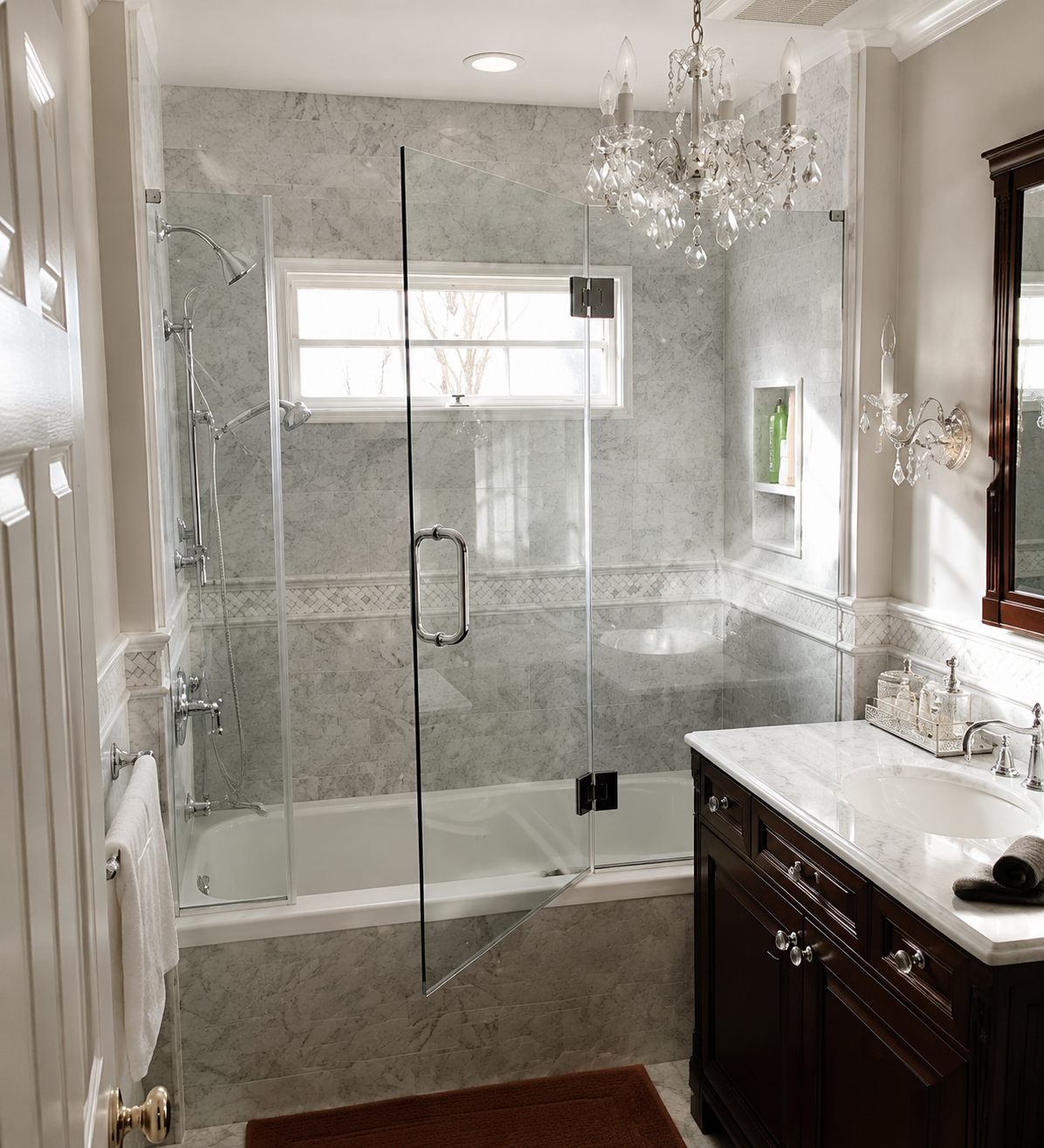 Elegant bathroom with glass shower, marble tile, chandelier, and dark wood vanity.