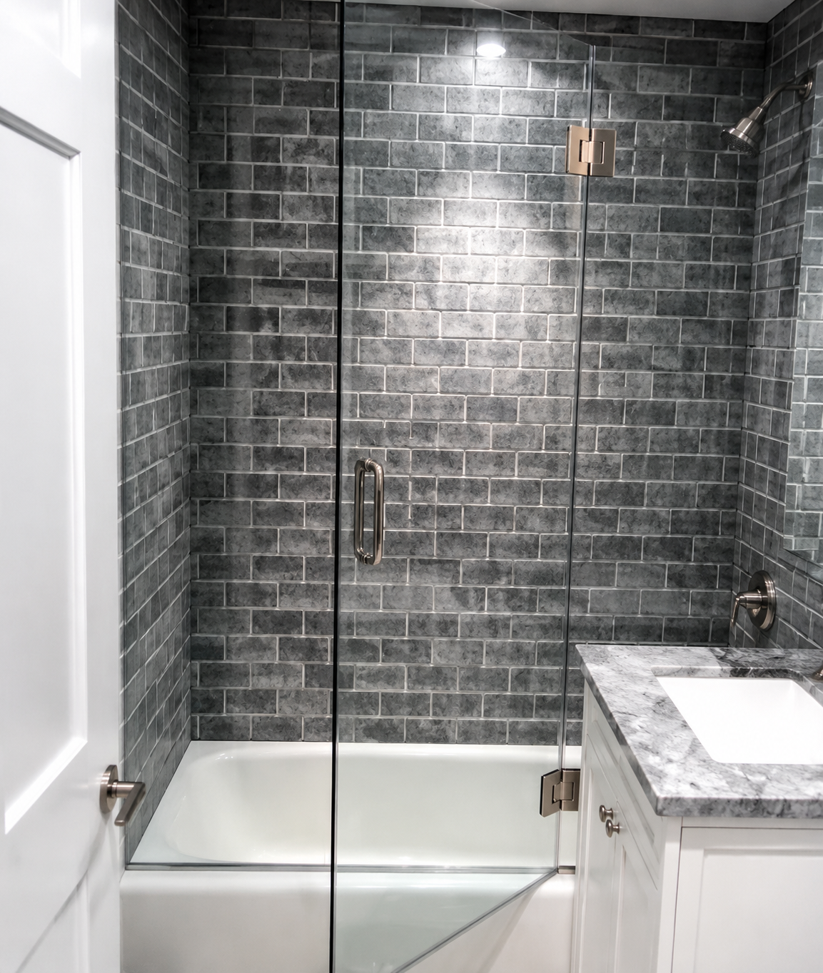 Modern bathroom with gray tile shower, glass door, bathtub, and white vanity countertop