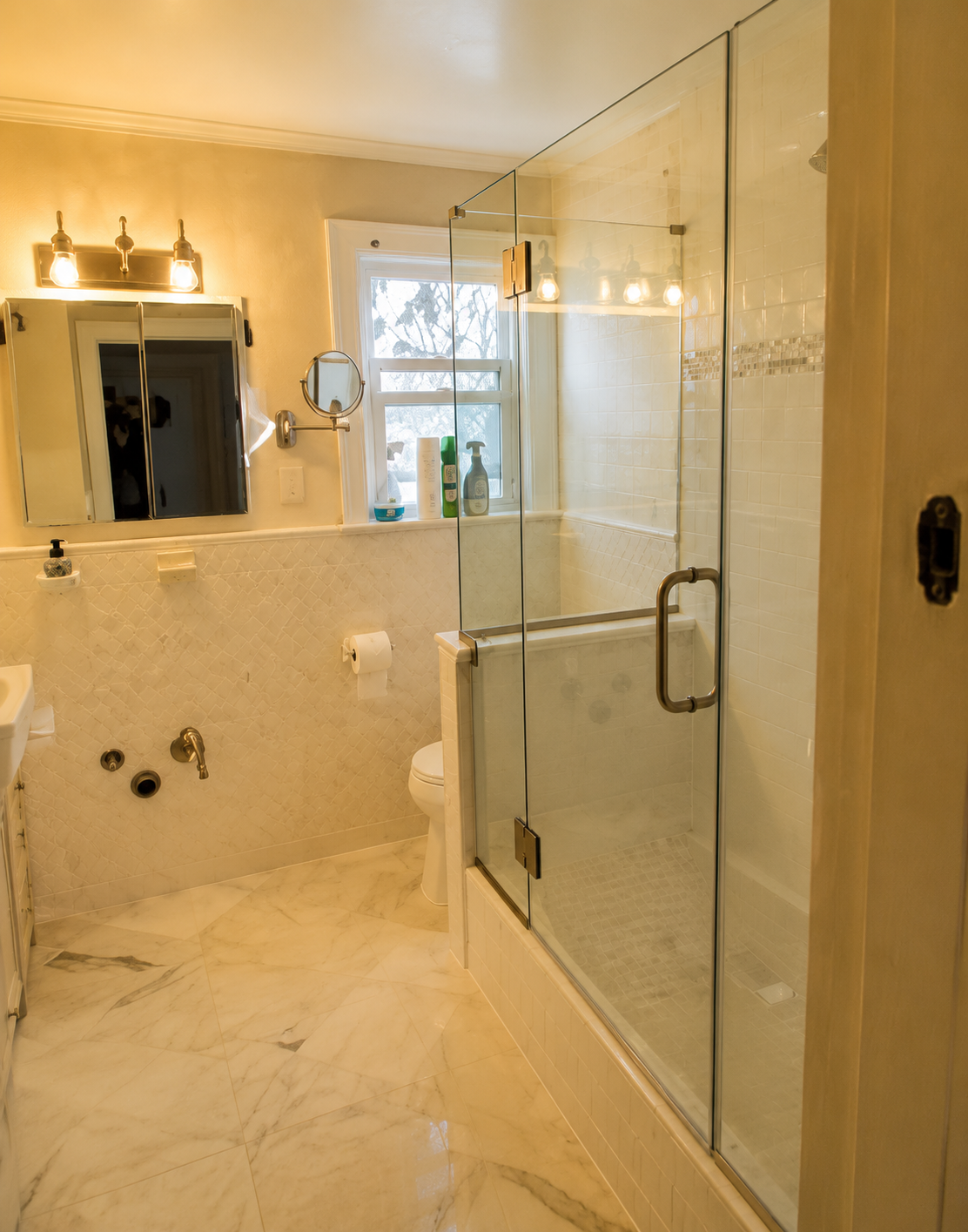 Luxury bathroom with marble tile, glass shower, vanity lights, and a windowed bathtub area