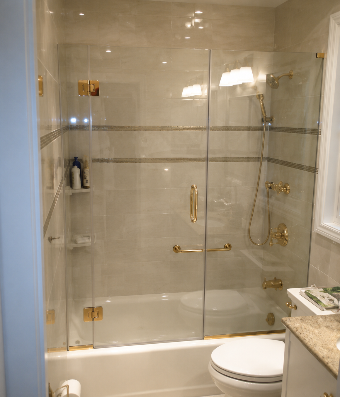 Glass-enclosed shower with gold fixtures next to a white toilet in a tiled bathroom.