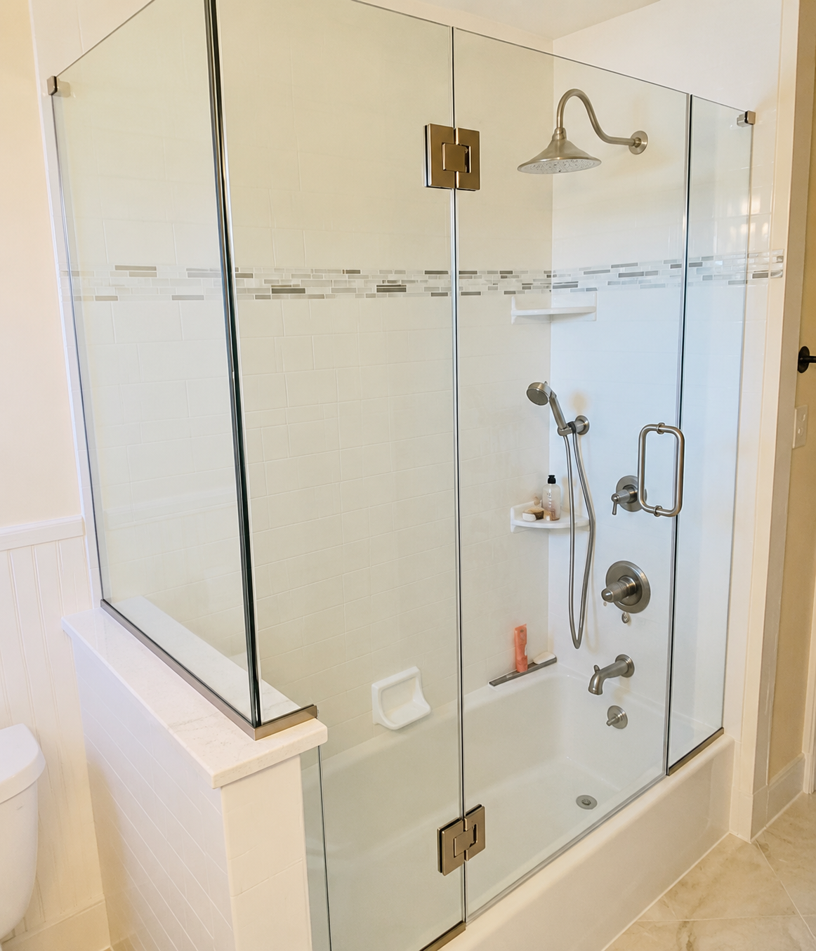 Glass-enclosed bathtub shower with chrome fixtures in a bright bathroom
