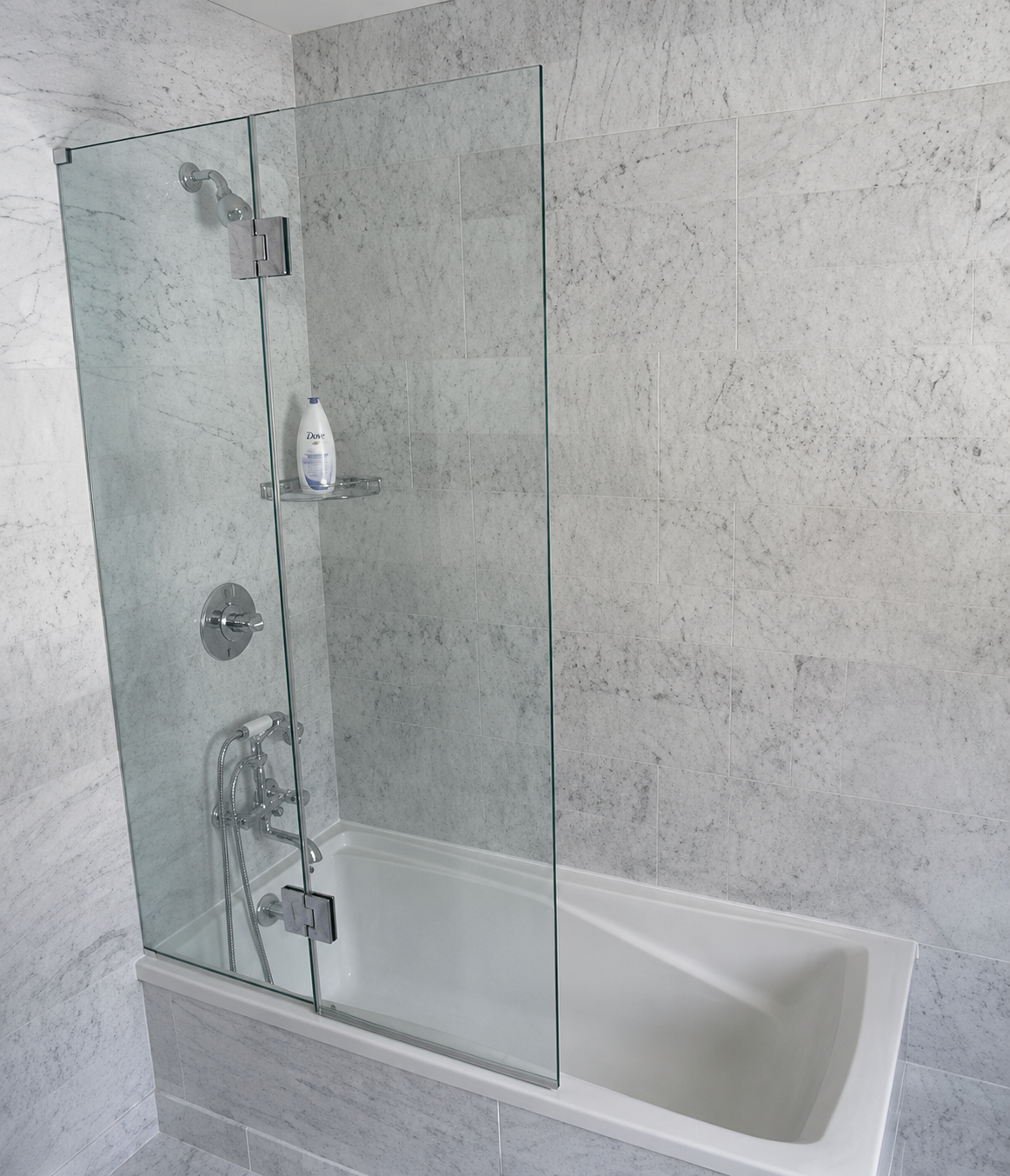 Modern bathroom with glass shower enclosure over a white bathtub and gray tile walls
