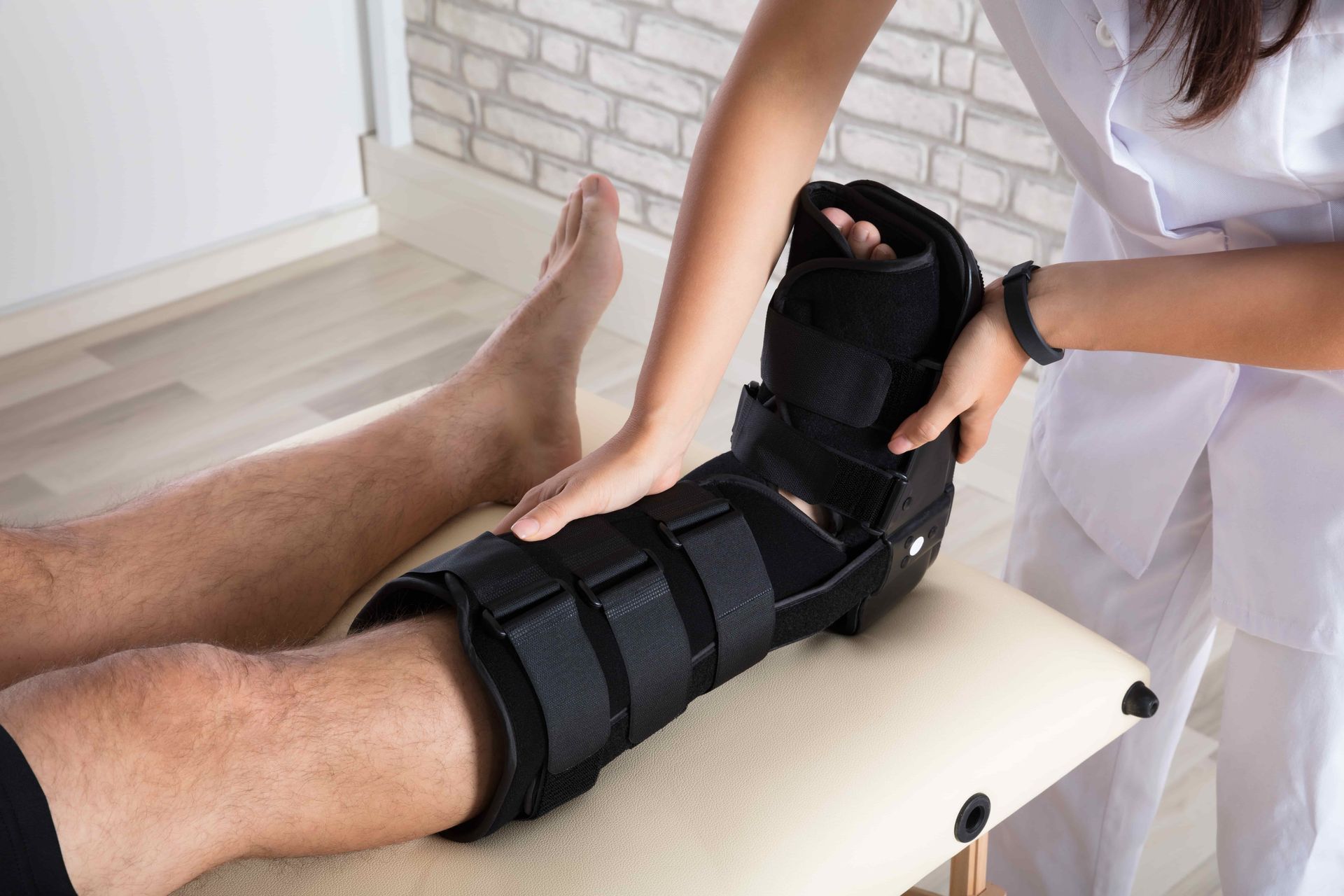 Therapist fitting a black leg brace on a patient’s lower leg during treatment
